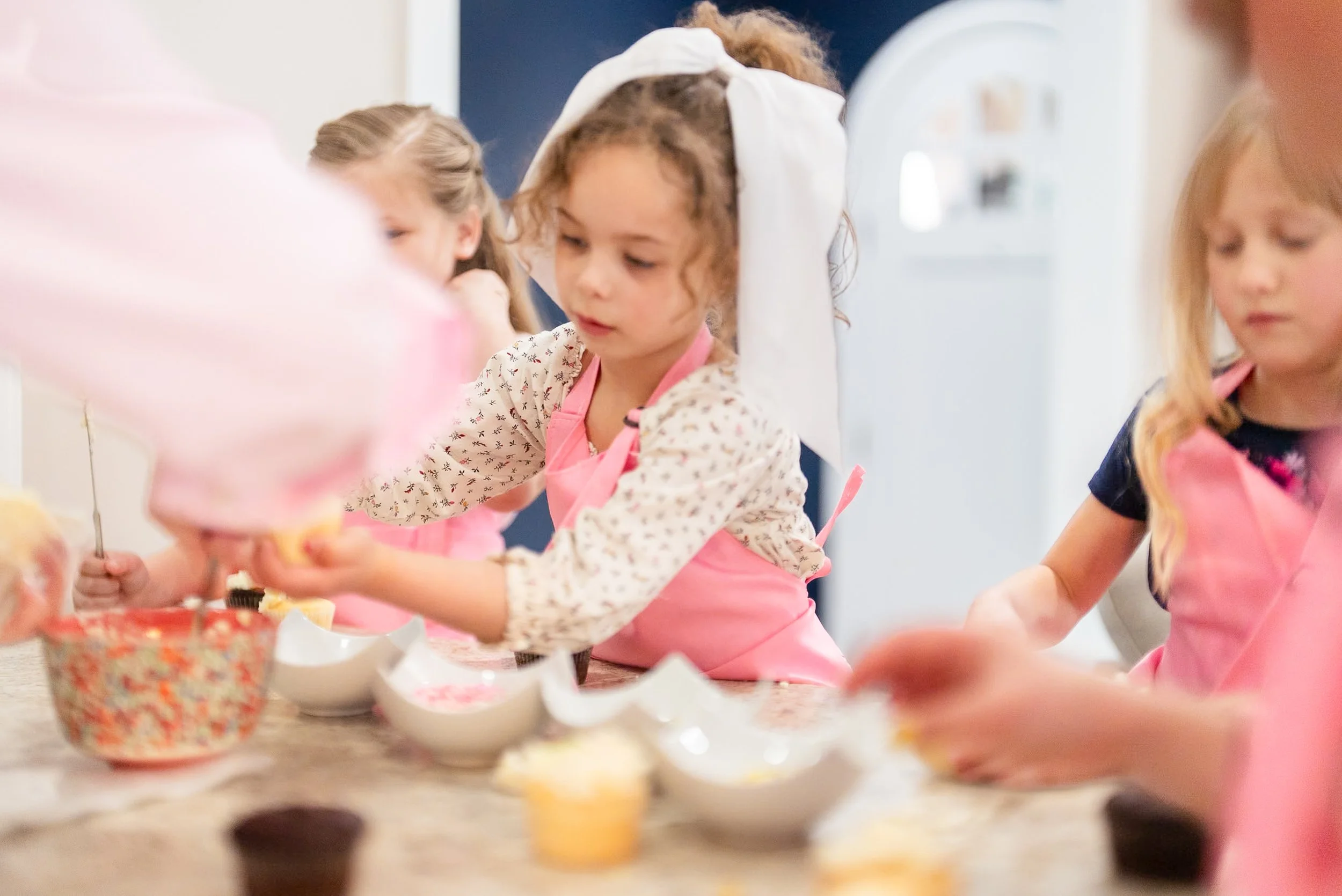 Children wearing pink aprons decorating cupcakes in a kitchen