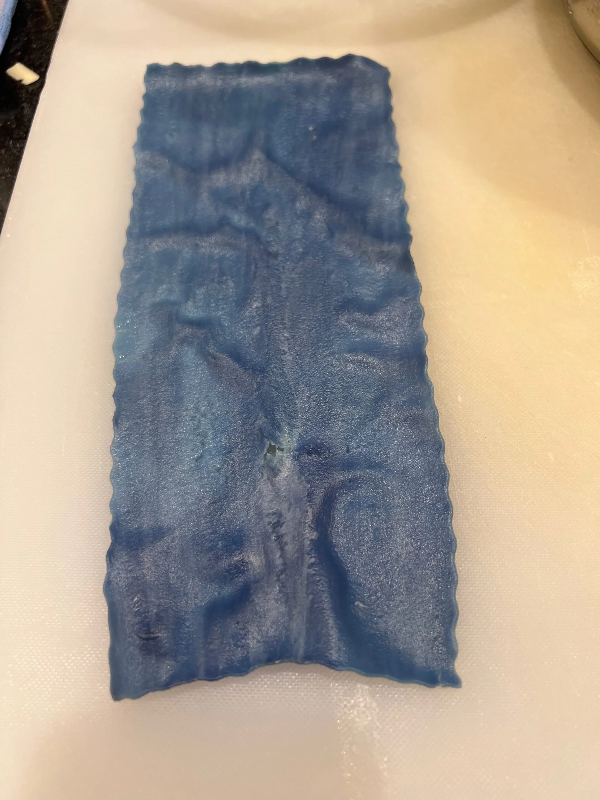 Blue rectangular sheet with a textured surface, placed on a white cutting board.
