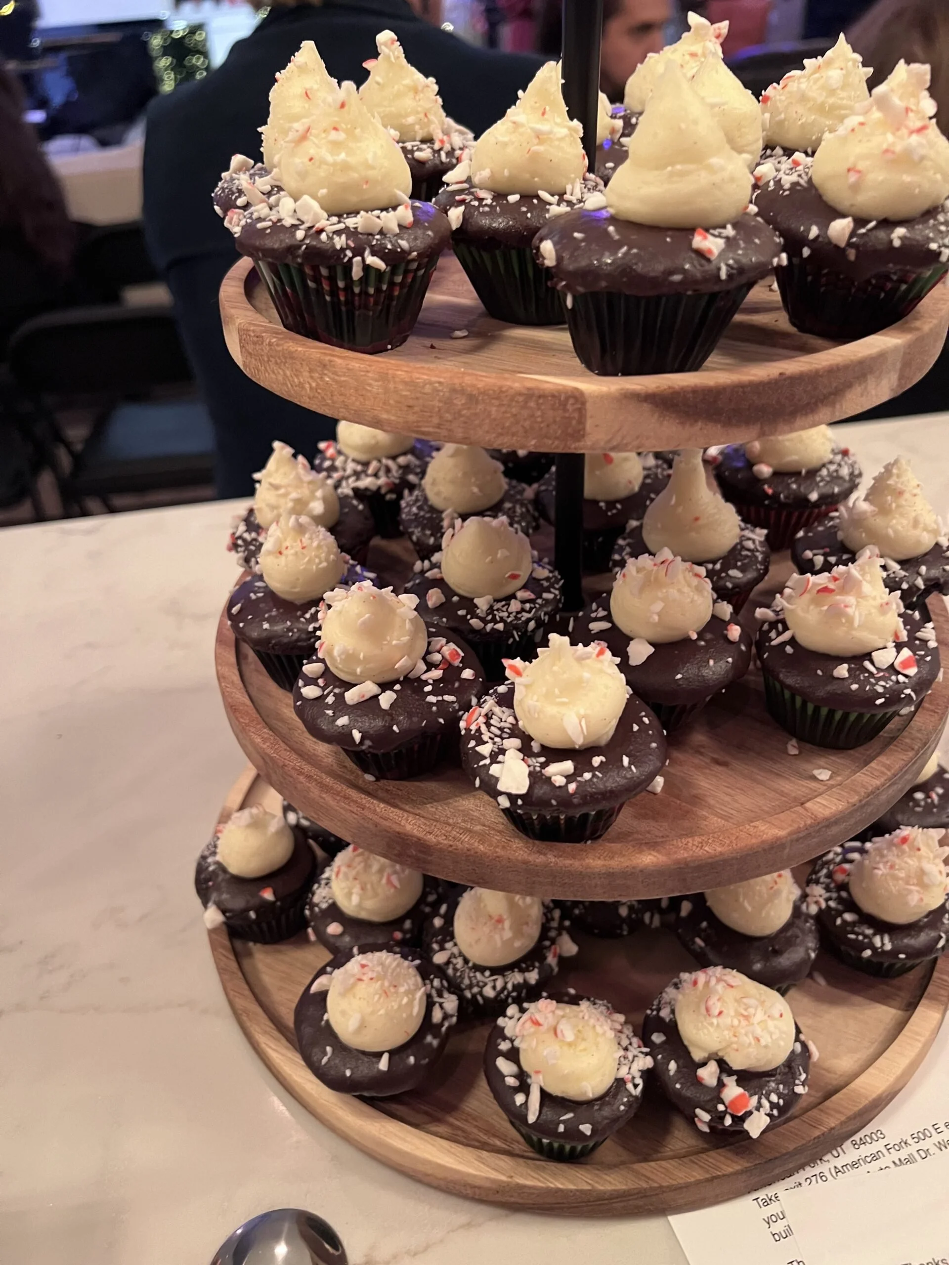 Assorted cupcakes decorated with white and red toppings on a three-tier wooden serving stand at a restaurant.