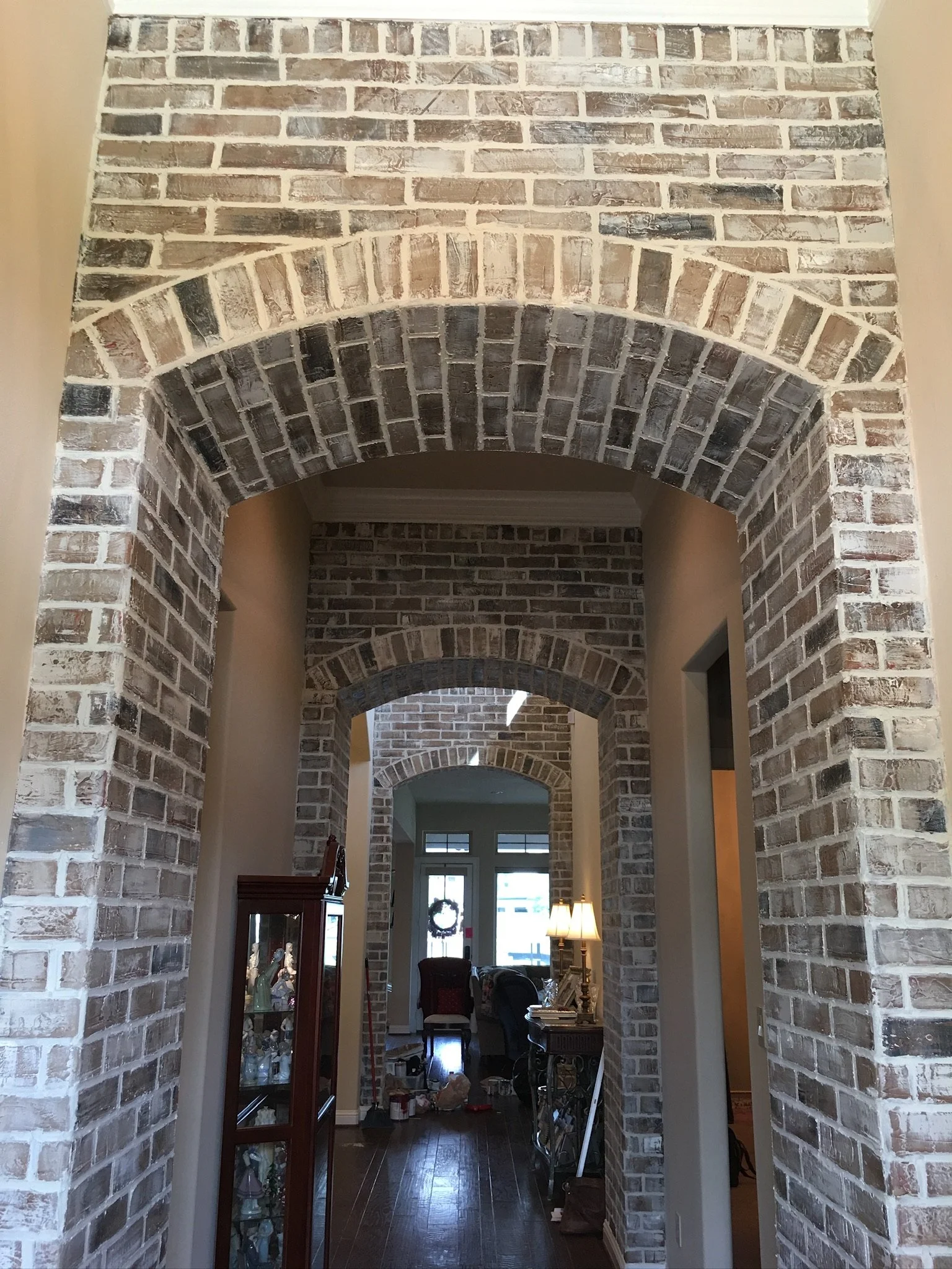 Interior view of a house with brick arches and hallway leading to a living room with furniture and decorations.