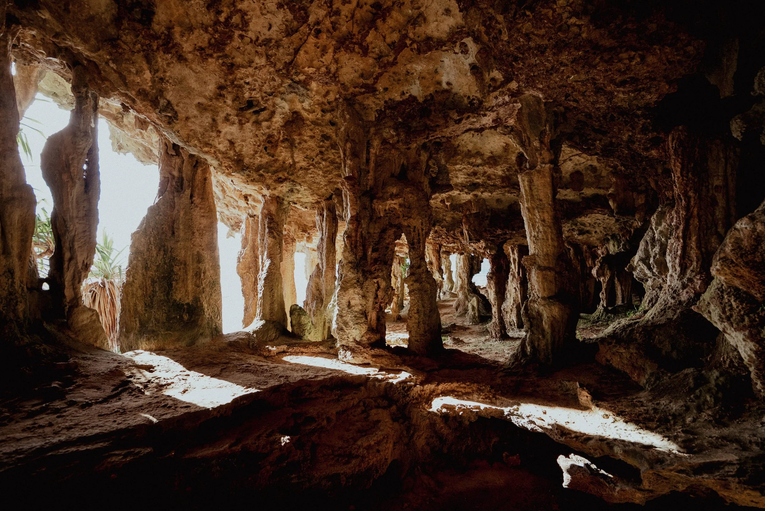 Caverne avec des stalactites, stalagmites et lumière naturelle entrant par des ouvertures dans la roche.