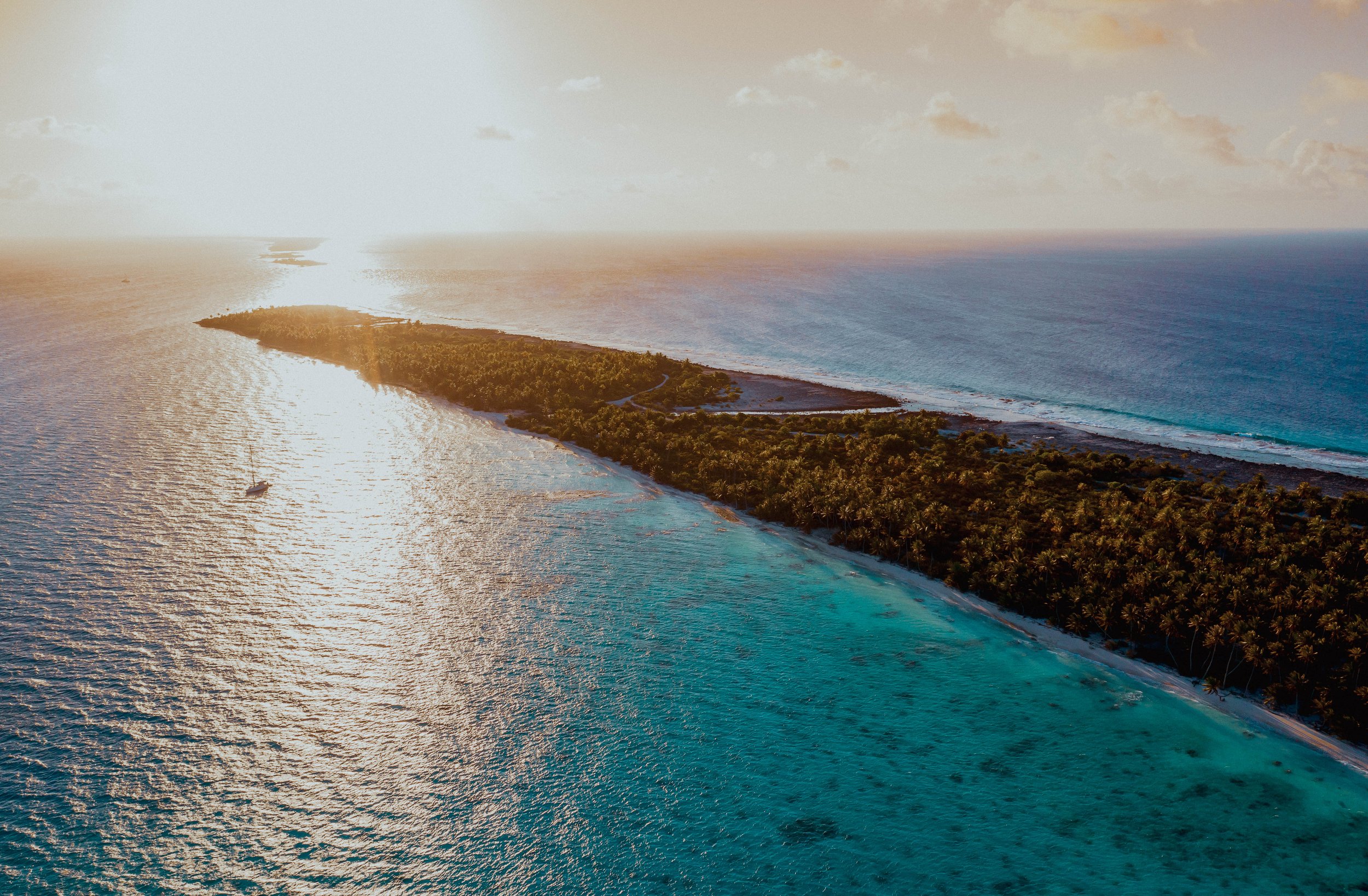 Vue aérienne d'une île tropicale avec une forêt dense, entourée d'eau turquoise et de plages de sable blanc au coucher de soleil