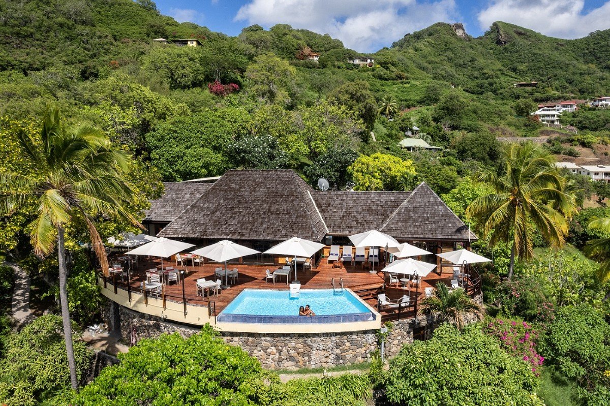 Villa avec piscine sur une terrasse en bois, entourée d'arbres tropicaux, avec vue sur une montagne verdoyante.