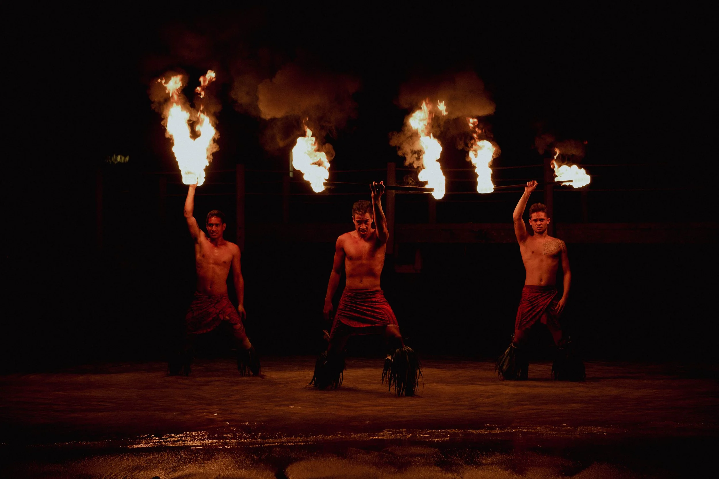 Marquisiens, portant des jupes rouges, jouent avec le feu lors d'un spectacle nocturne dans une baignoire d'eau.