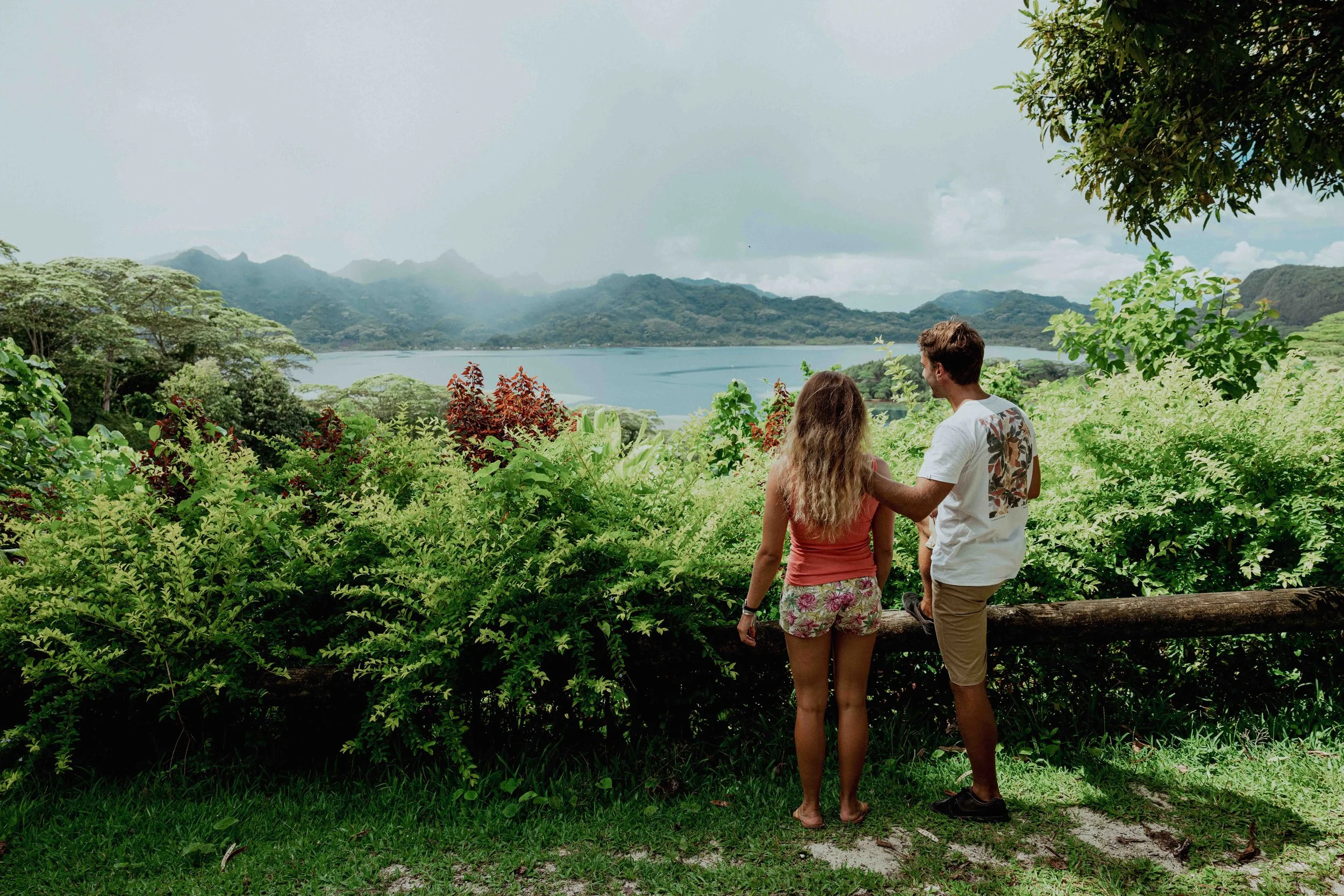 Un couple regarde un lac entouré de montagnes verdoyantes dans une nature luxuriante.