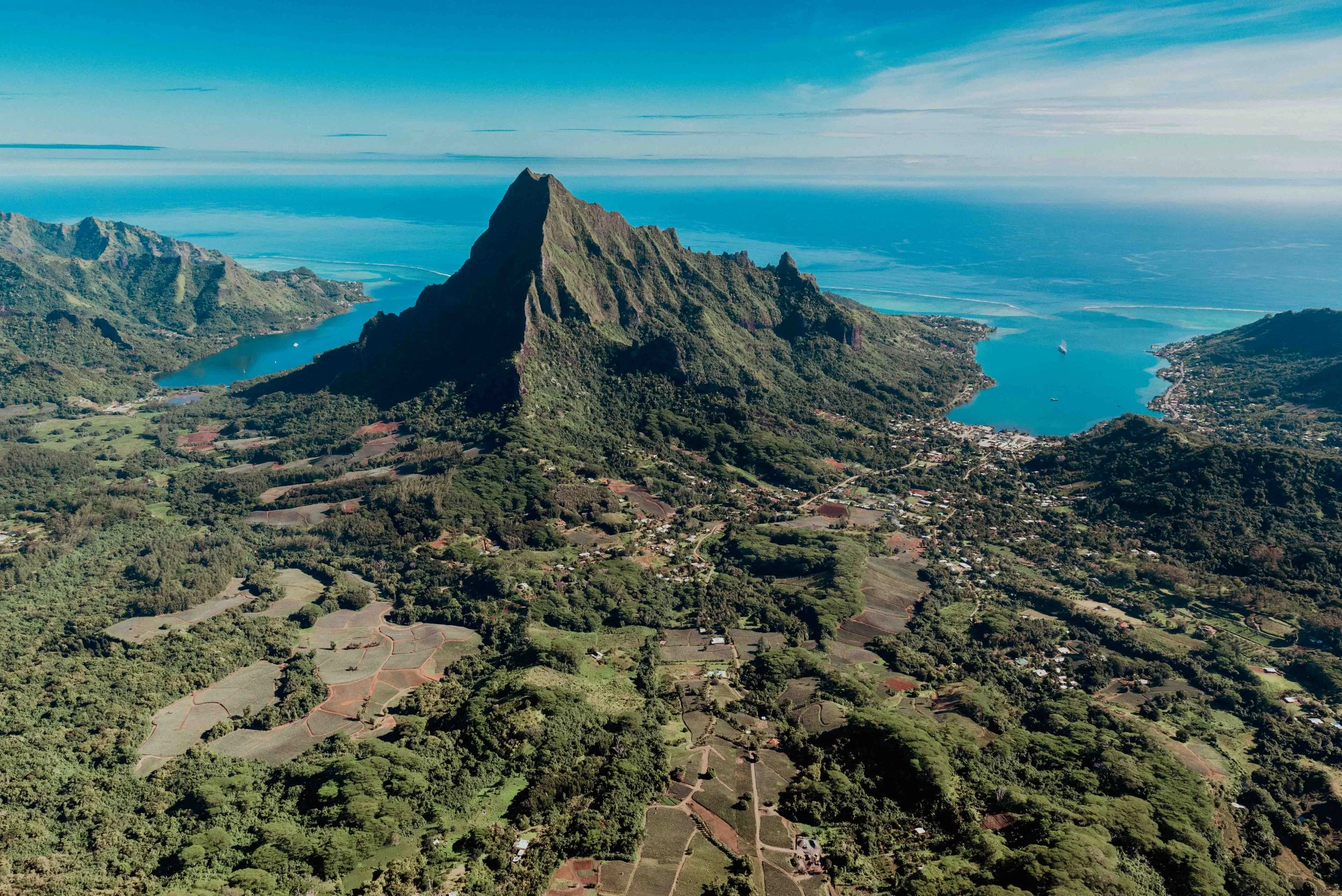 Vue aérienne d'une montagne en pyramide entourée de forêts, d'îles, de lacs et de l'océan avec un ciel bleu dans un paysage tropical.