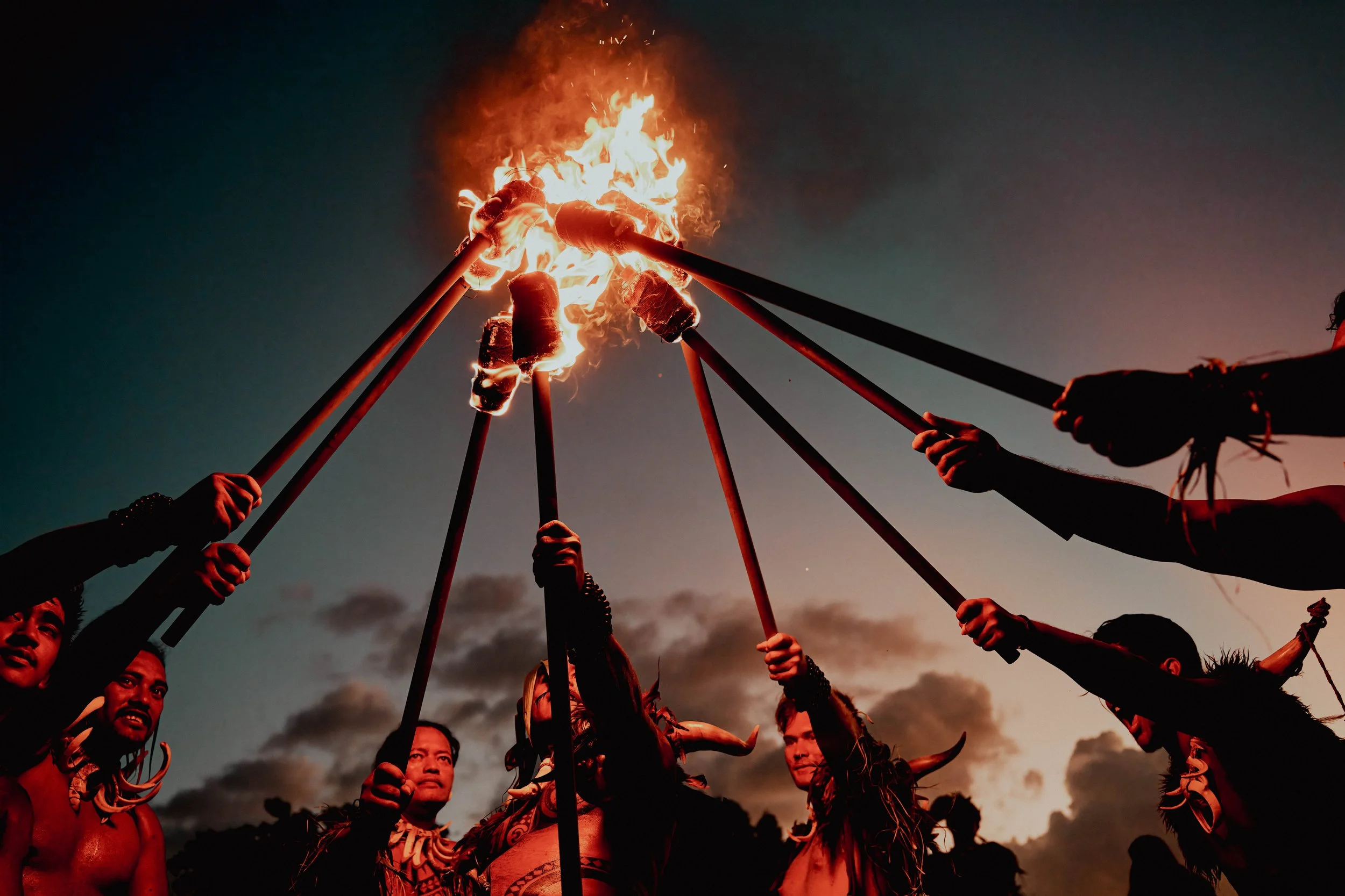 Marquisiens, portant des ornements traditionnels, tenant des bâtons avec des torches enflammées lors d'une cérémonie au crépuscule.