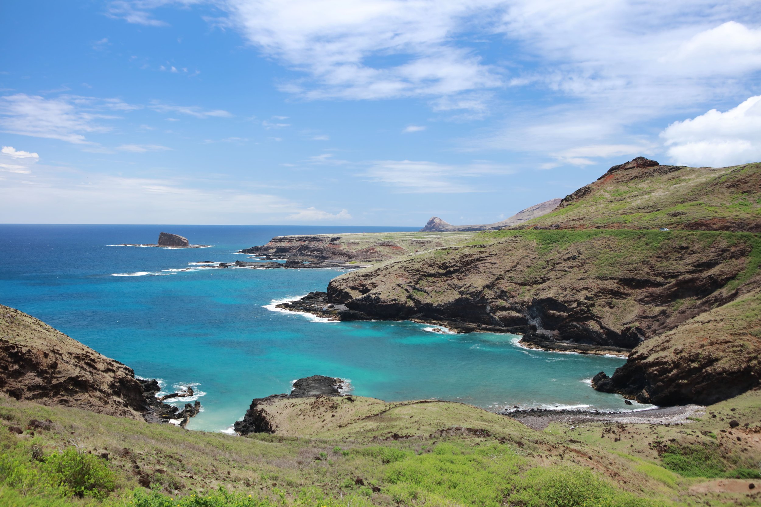 Paysage côtier avec des falaises escarpées, une plage et une mer bleue turquoise, sous un ciel partiellement nuageux.