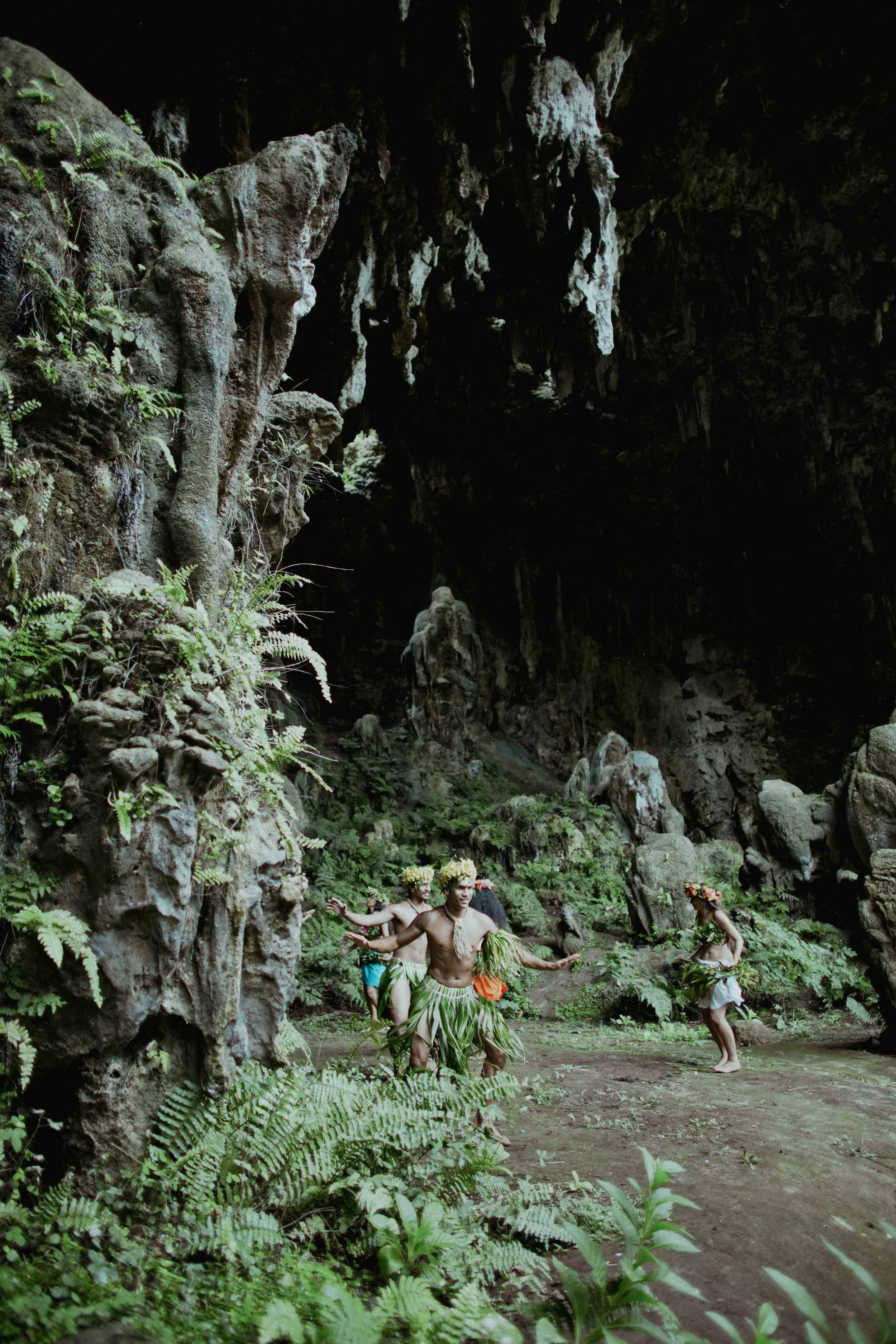 Groupe de personnes en costumes traditionnels dans une grotte avec végétation et formations rocheuses.