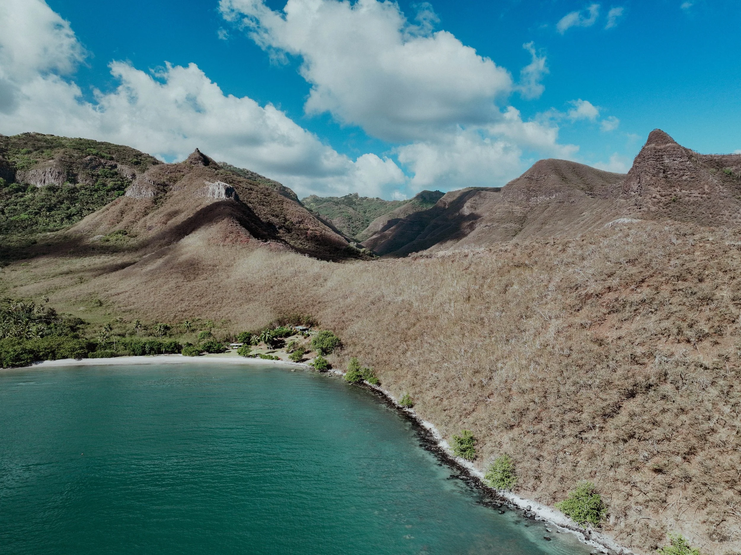 Côte rocheuse avec une mer turquoise, montagnes sèches et surréalistes, ciel partiellement nuageux.