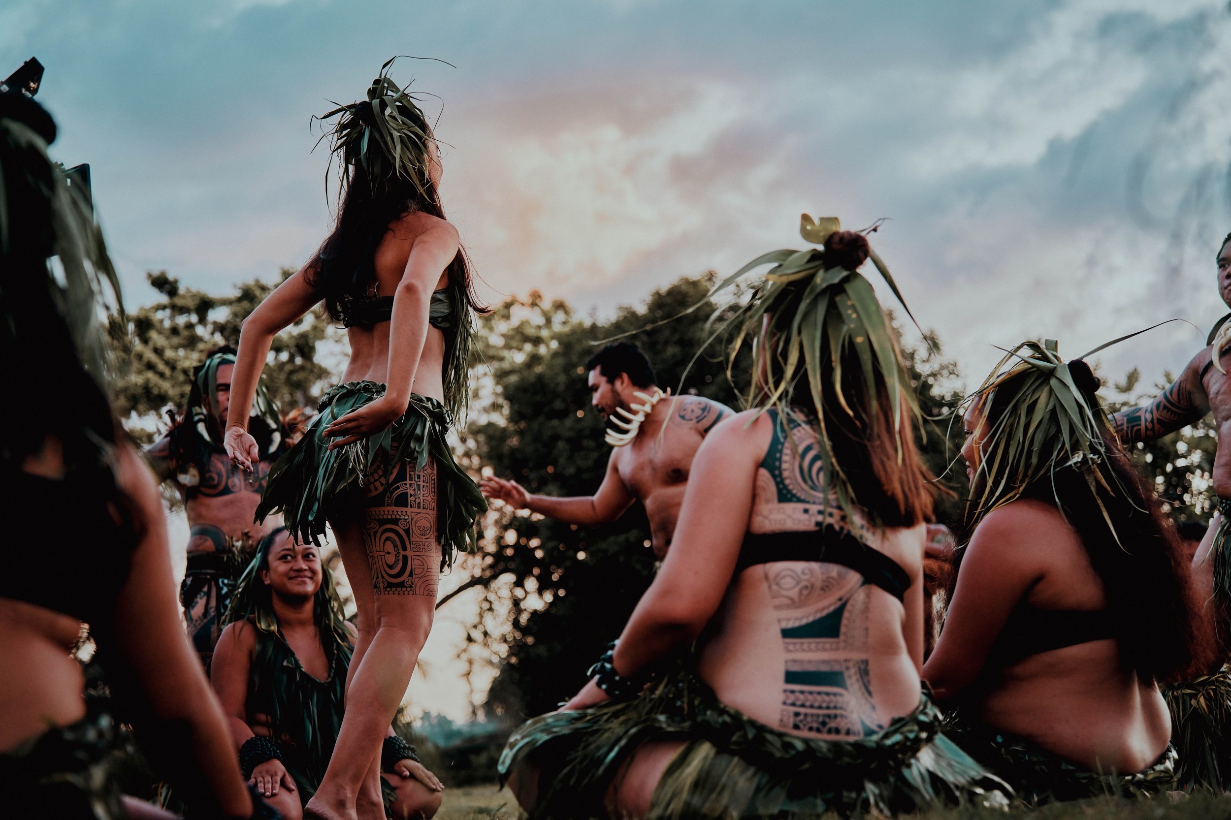 Marquisiens lors d'une cérémonie traditionnelle, portant des tenues en feuilles et des tatouages, sous un ciel nuageux.