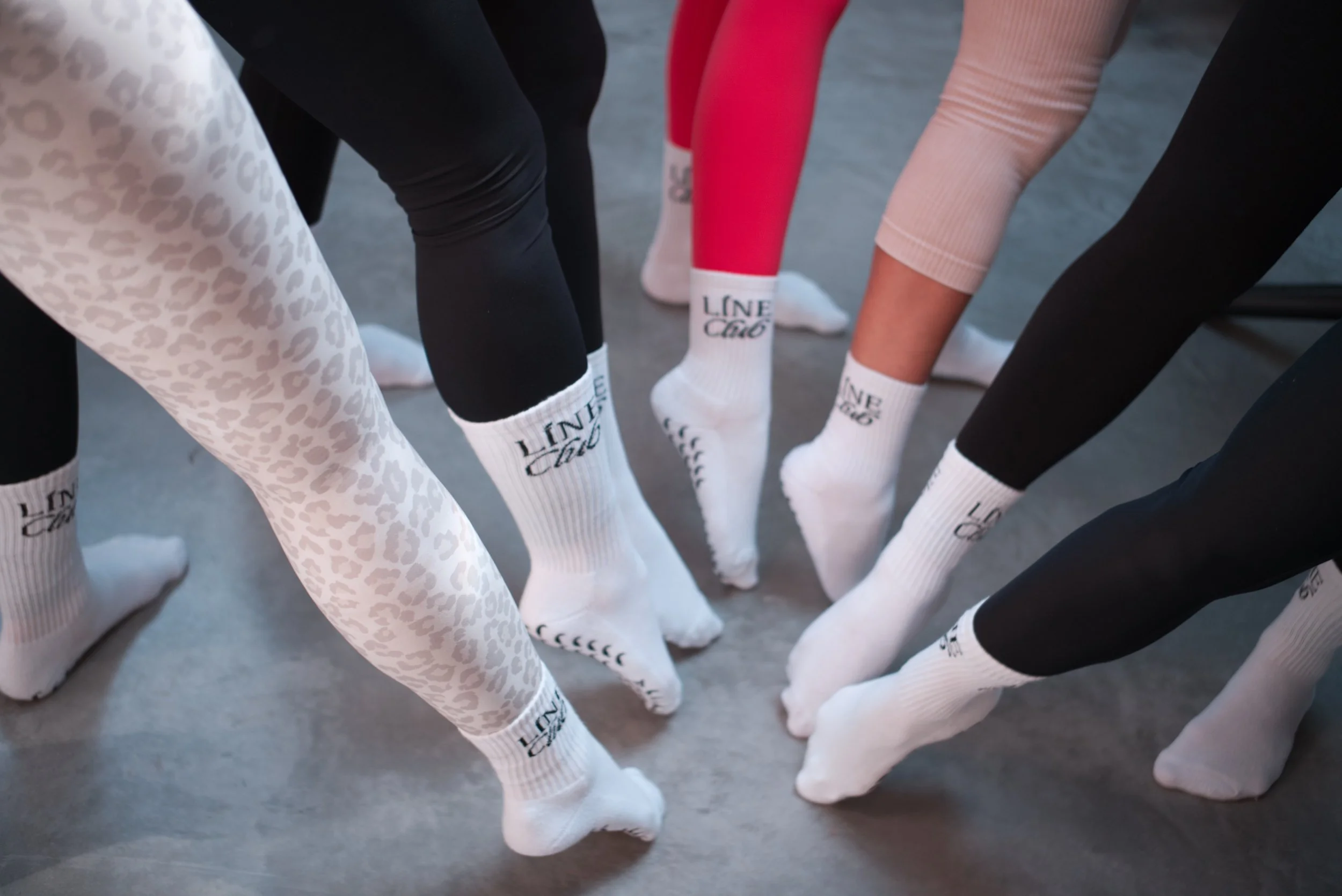 Menschen in verschiedenen Leggings sitzen im Kreis, tragen weiße Socken mit dem Schriftzug "Line Cafe".