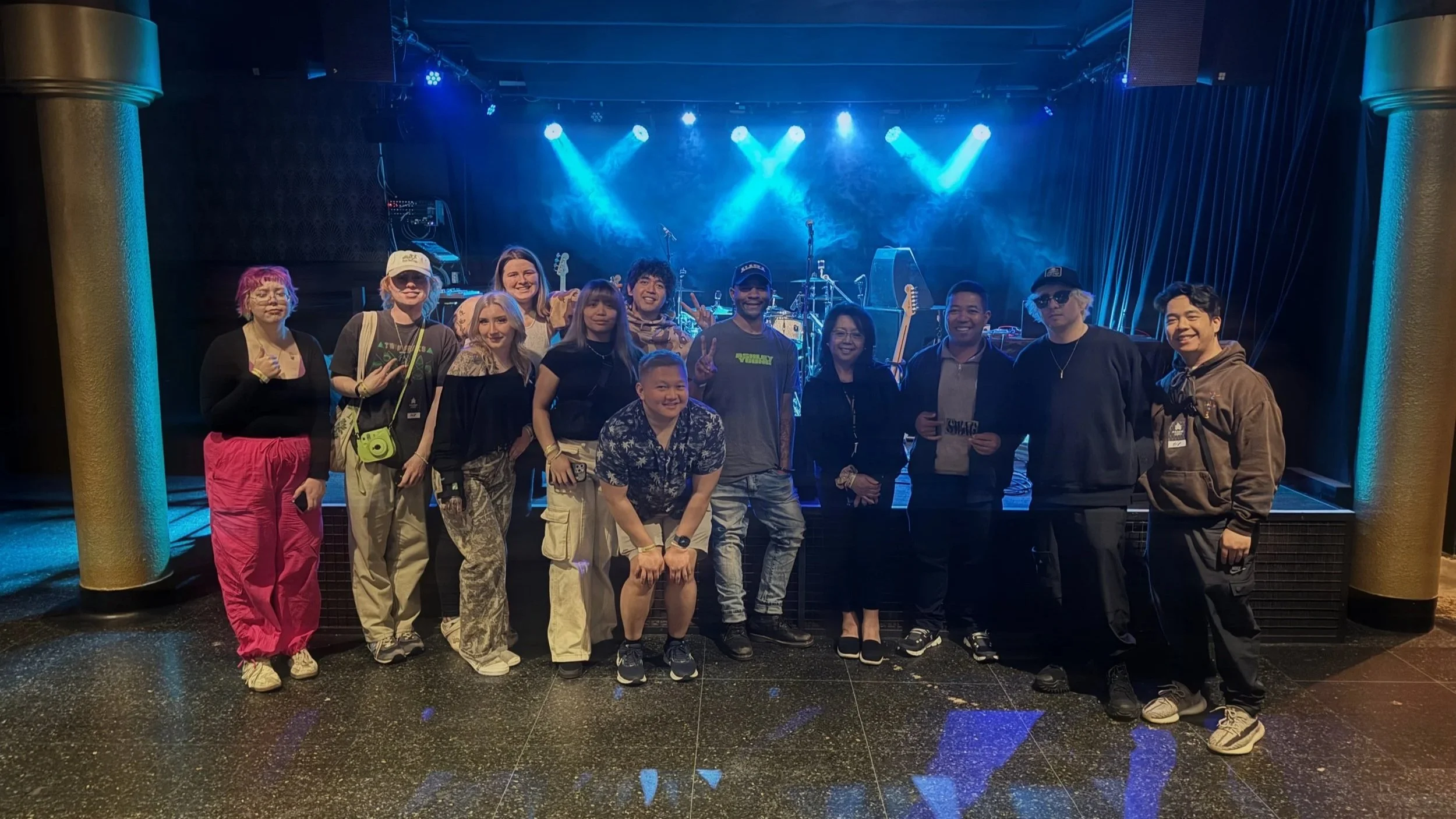 Group of people pose on stage with musical instruments and blue stage lights in the background.