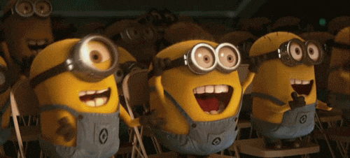 Three Minions with goggles and overalls smiling and laughing indoors.