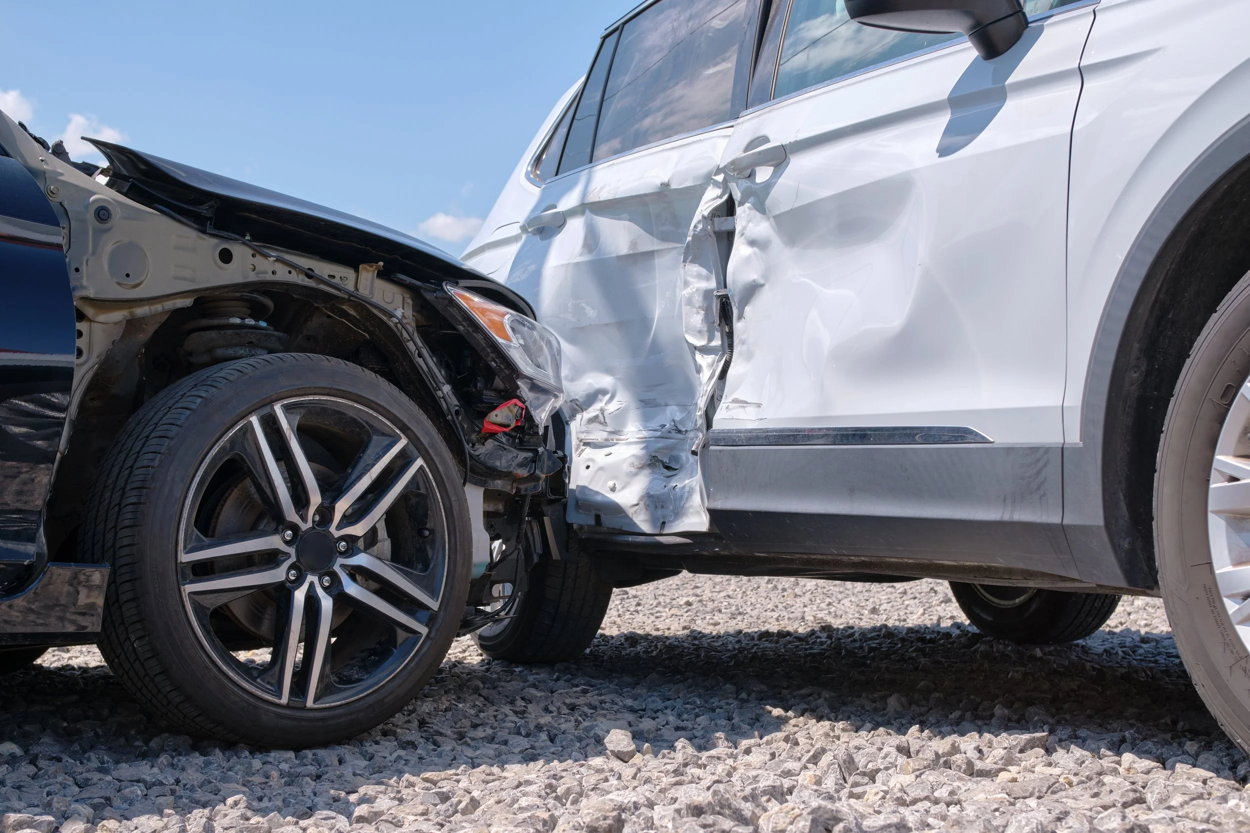 Two cars involved in a front-end collision; the black car's front is damaged and crumpled, and the white car has significant damage to its side door and panel.
