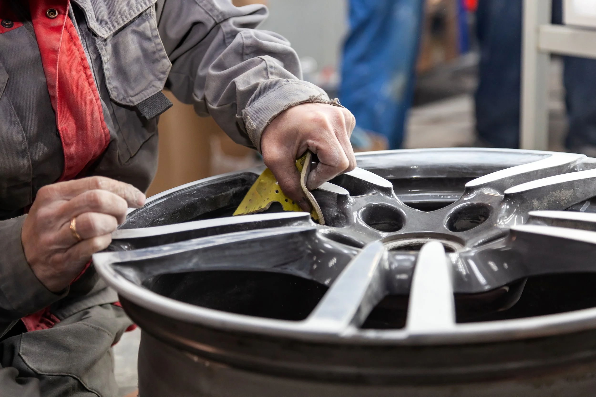 A person working on a car wheel rim, using a tool to clean or polish it in a workshop.