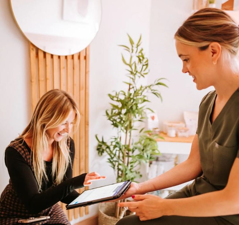 A woman receiving a tablet from a healthcare professional in a brightly lit, modern medical office with a plant in the background.