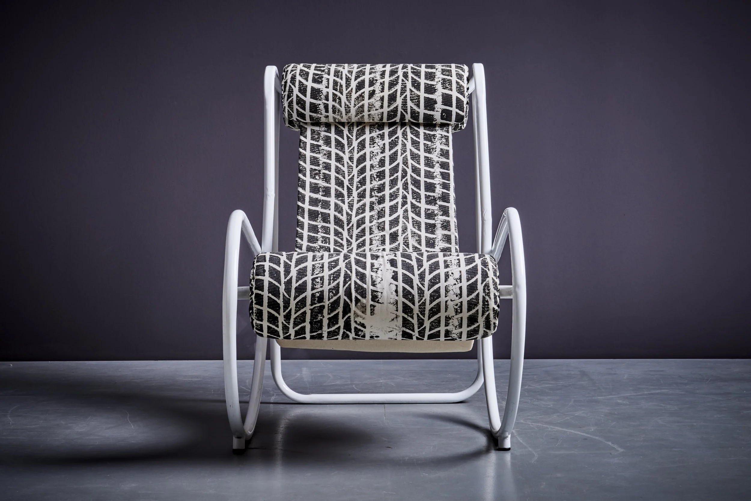 Black and white patterned chair with a white metal frame against a dark wall
