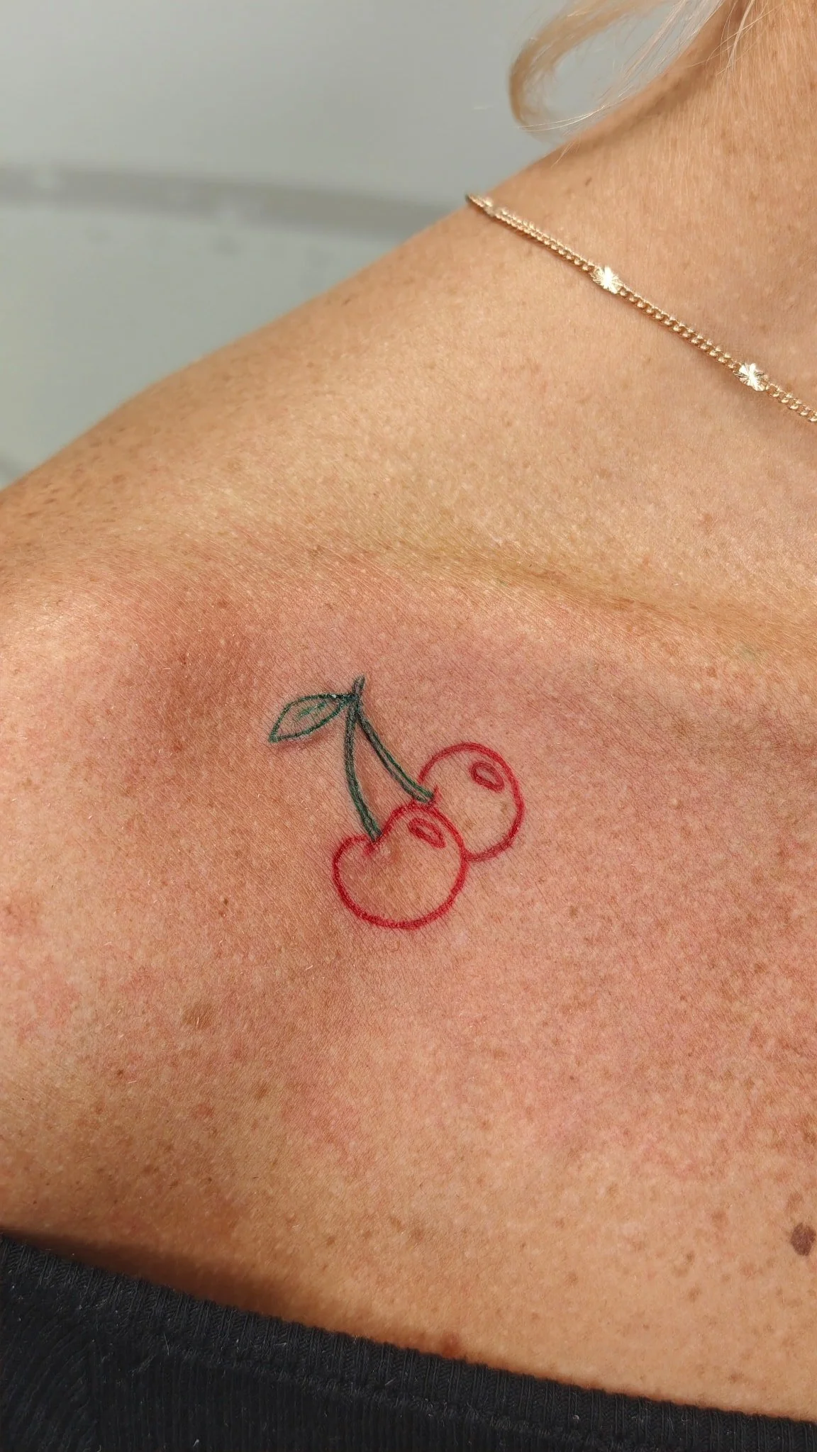 A tattoo of two cherries with green leaves on a person's shoulder.