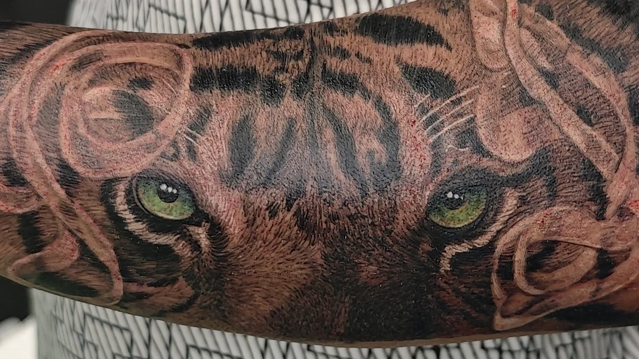 Tigro snukio tatuiruotė su žaliomis akimis ant rankos.