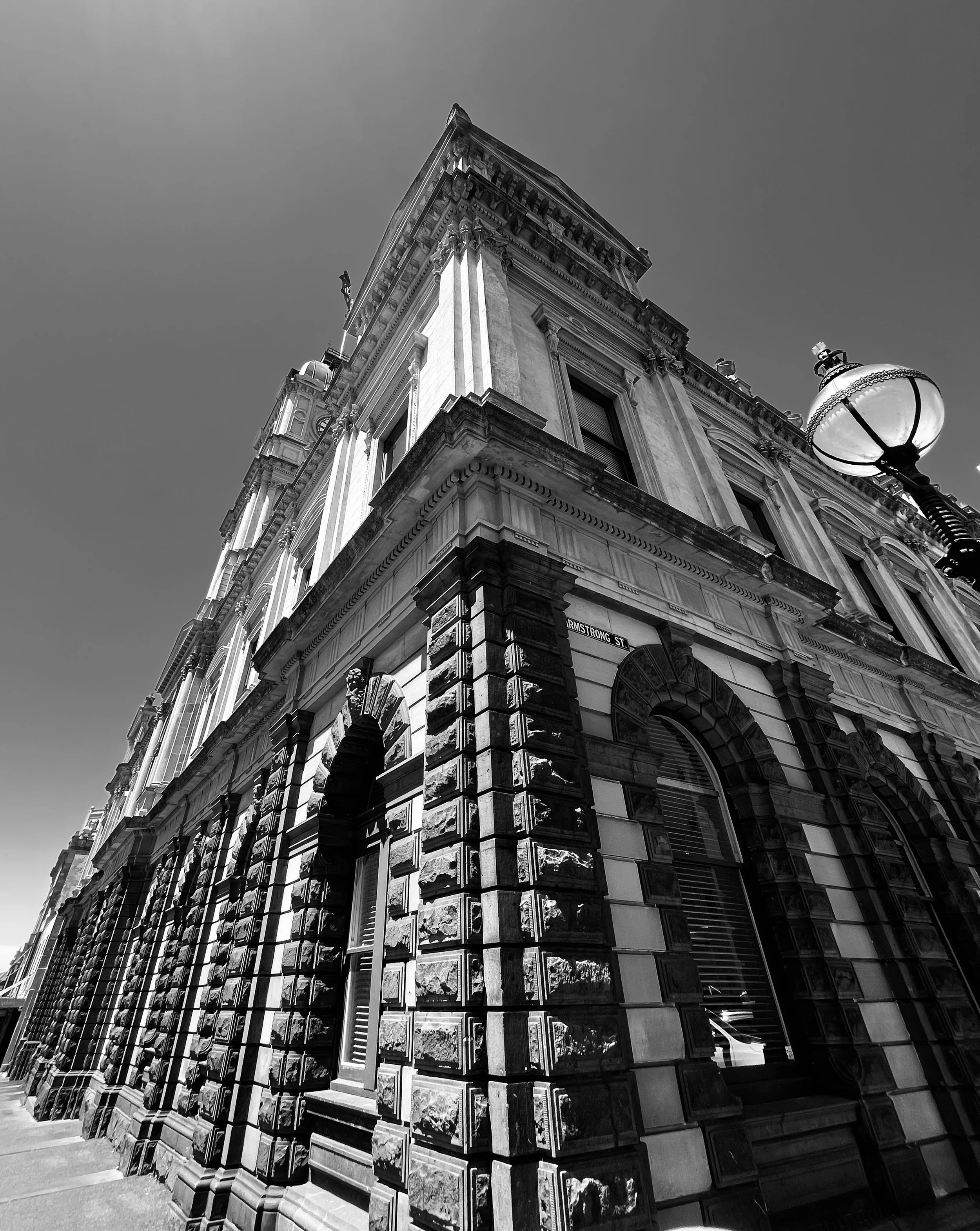 Black and white photo of an ornate historic building with detailed stonework, arched windows, and a streetlamp on the corner.