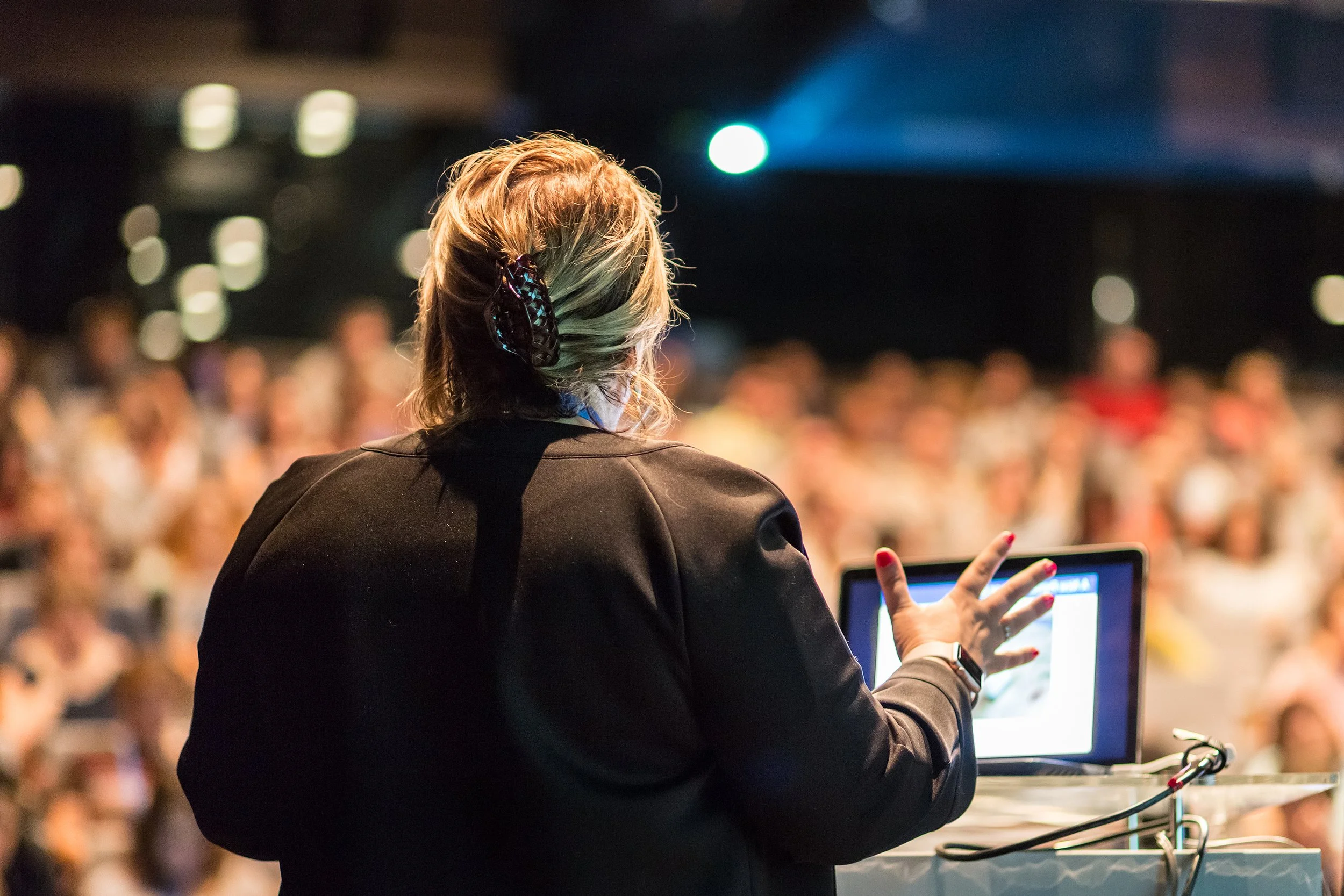 Woman in black blazer giving presentation to large crowd
