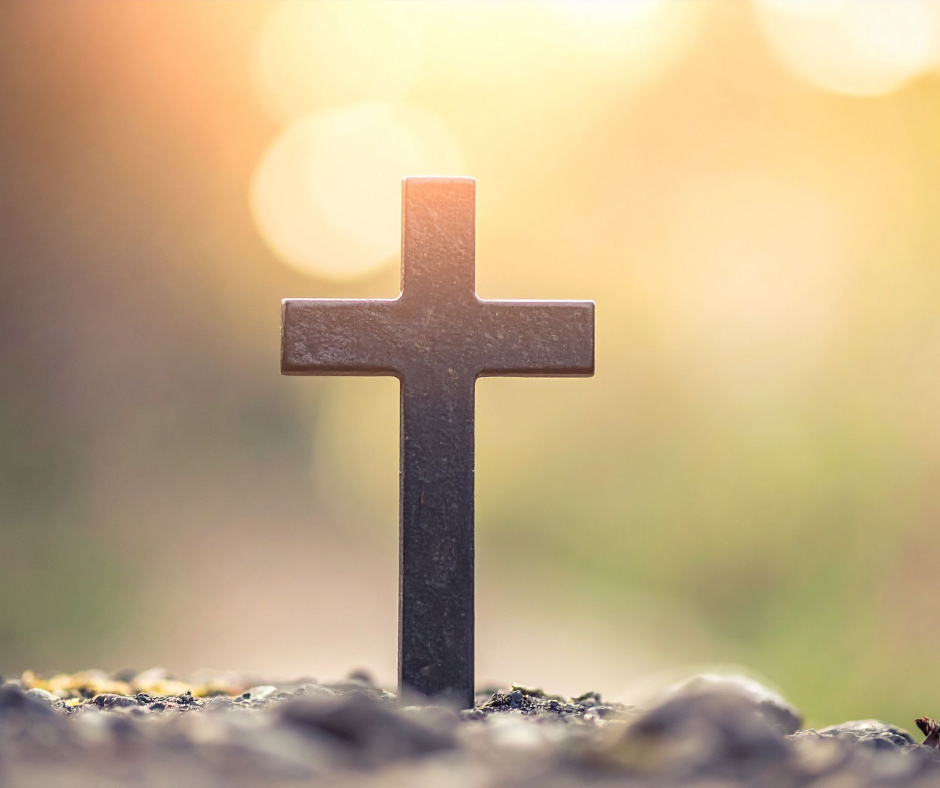 A cross monument on the ground with blurred warm sunlight background.