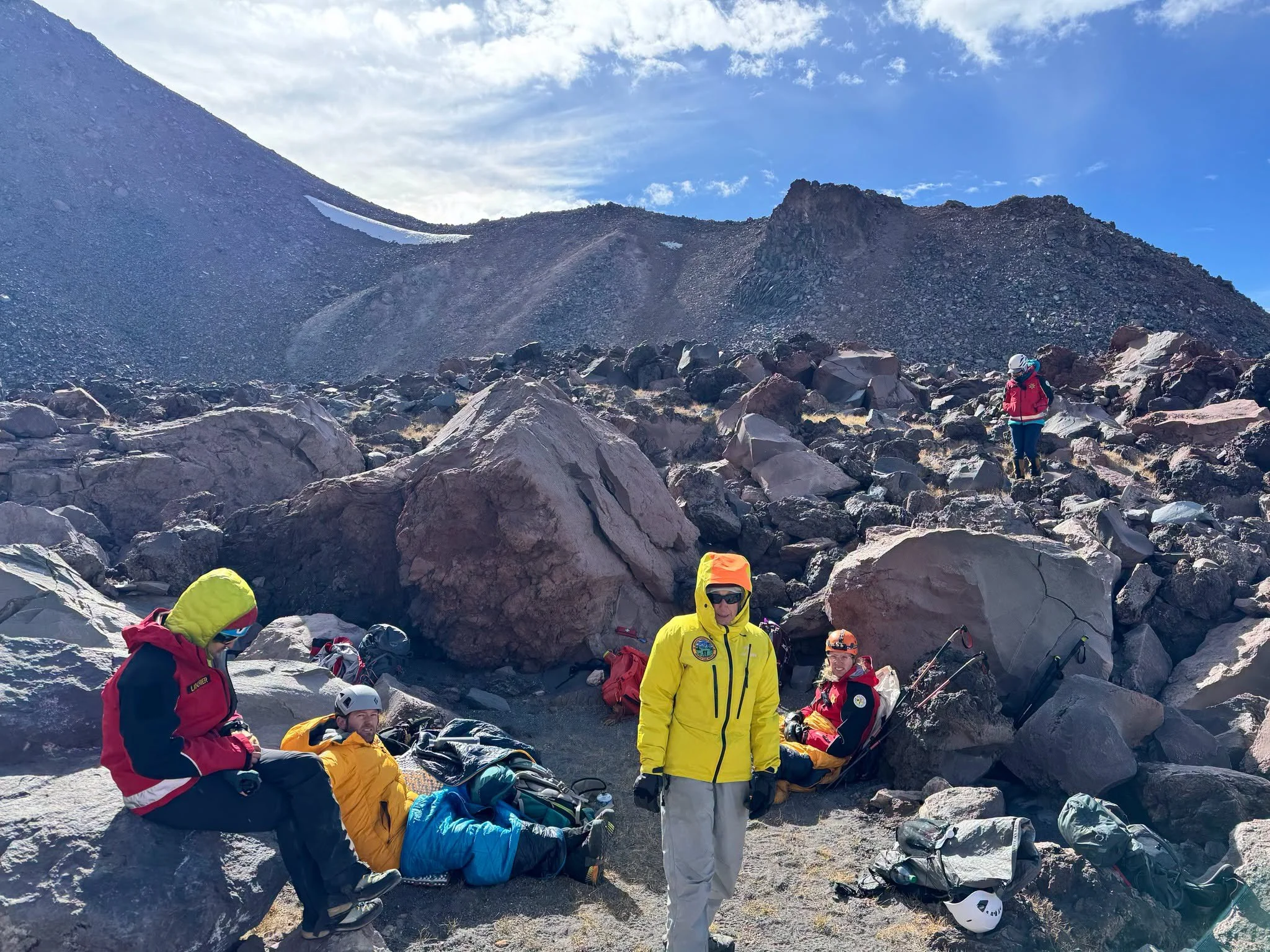   Climber Receives Aid on Mount Shasta:  Rescue personnel gather with an injured climber in a sheltered area among large volcanic boulders. Forest Service climbing rangers provided emergency assistance after reaching the man Monday morning and remain