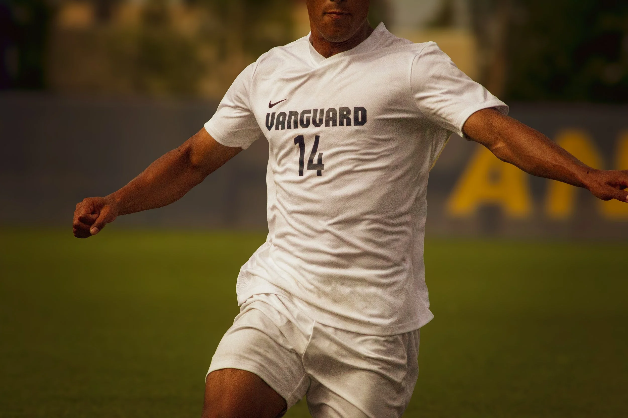 A soccer player is shown mid-action, wearing a white jersey with 'Vanguard' and the number 14, on a green grassy field.