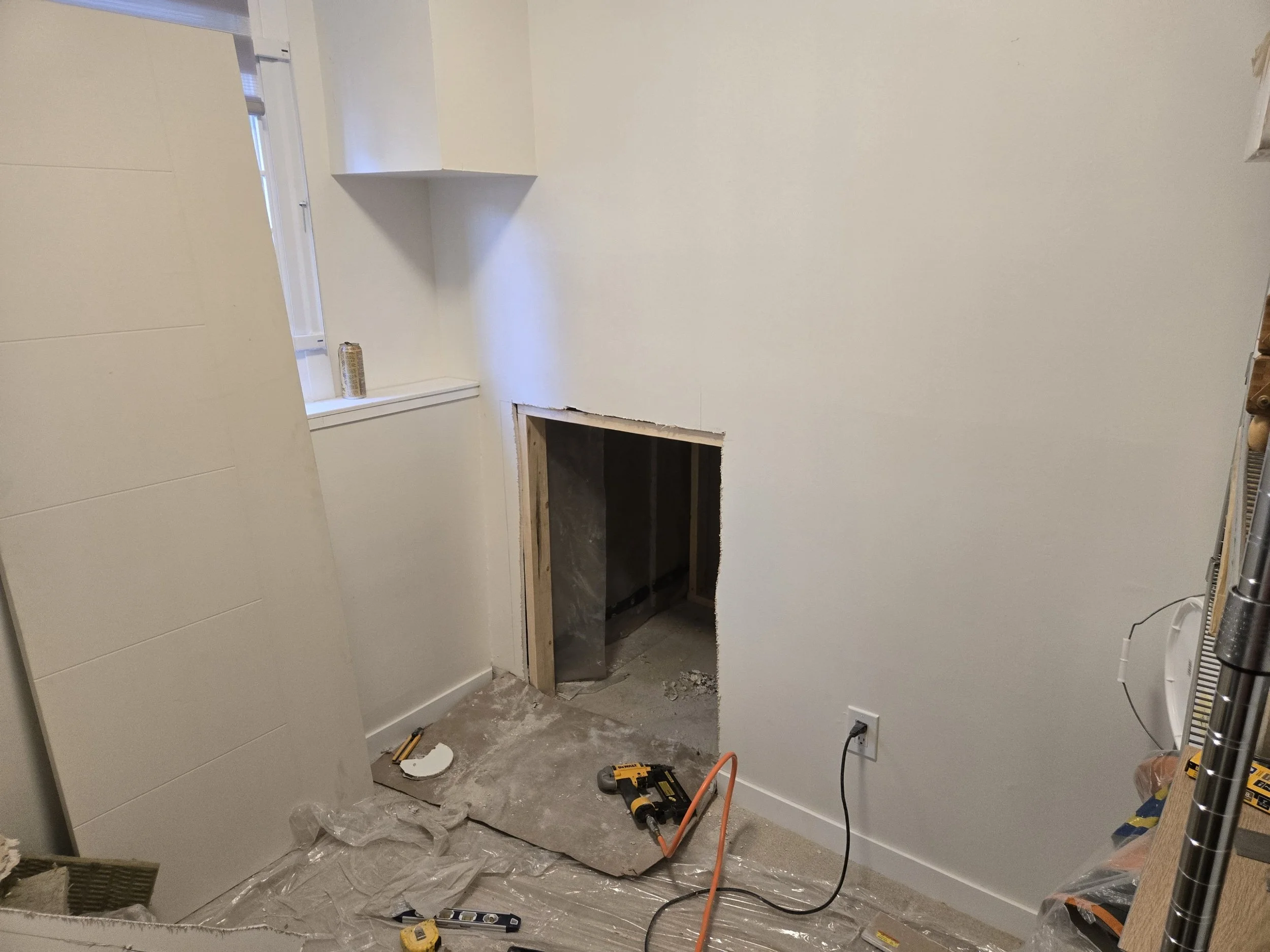 Room under renovation with a hole in the wall, tools on the floor, and construction materials around.