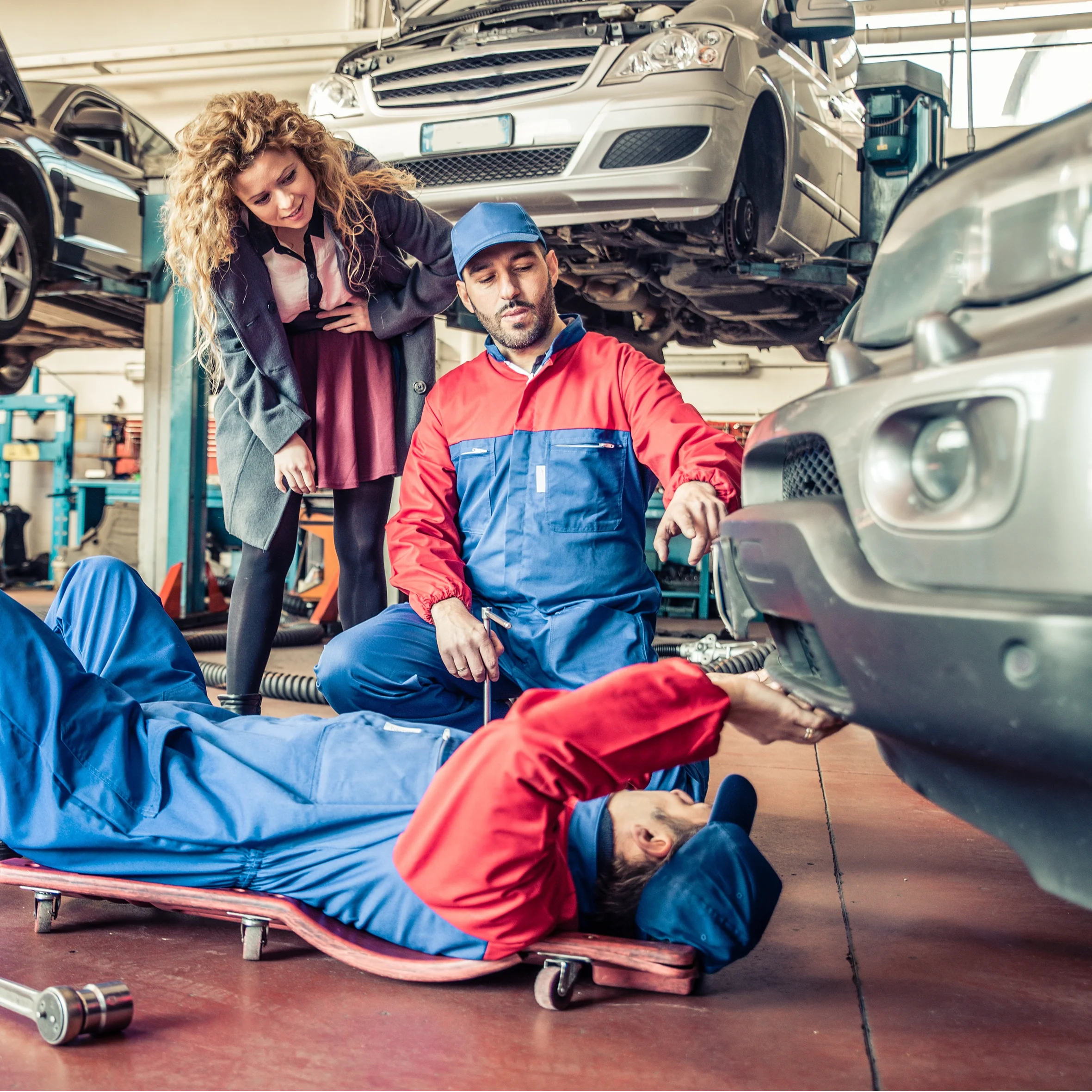 Mechanics in blue and red coveralls showing a female customer repairs needed on her car