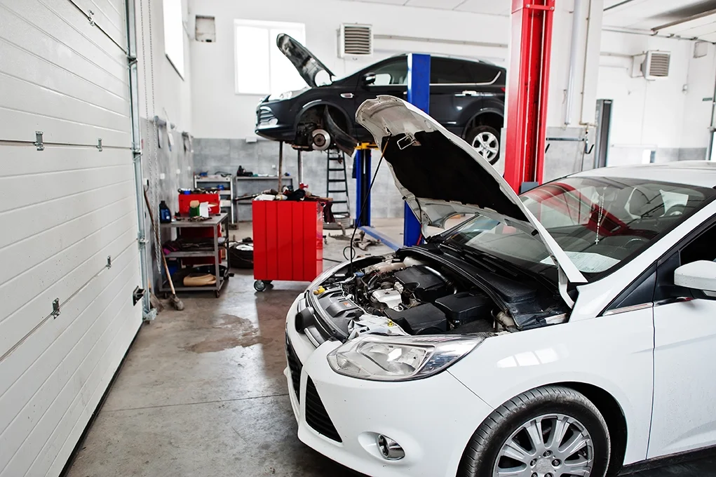 Inside auto repair shop - white car with hood open and black car with hood open on lift in the background