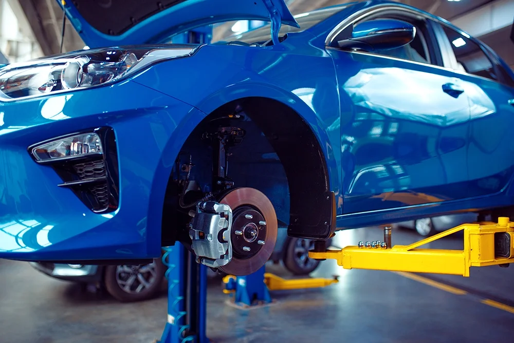 Blue sedan with wheel removed on lift auto repair service.webp