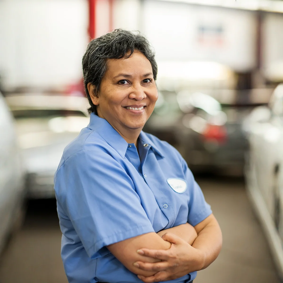 Smiling hispanic female folded arms mechanic blue uniform shirt