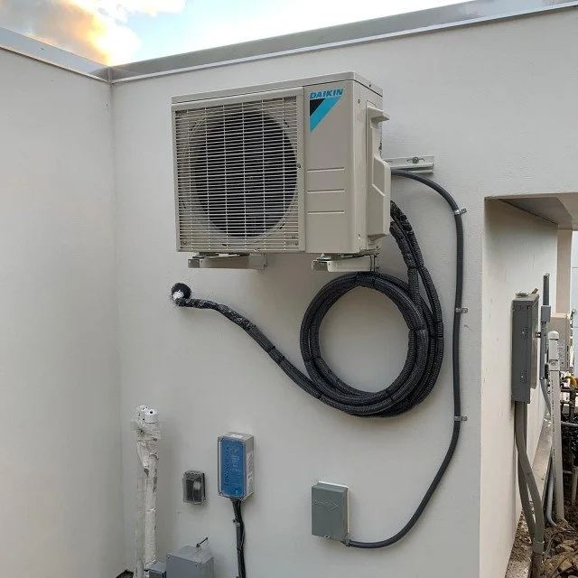 Exterior wall with a Daikin air conditioning unit, electrical boxes, and conduit pipes.