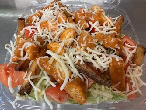 Salad with grilled chicken, shredded cheese, tomato, and orange-colored dressing in a plastic container.