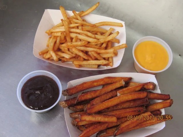 French fries with two dipping sauces, one dark and one yellow, on a metal table.