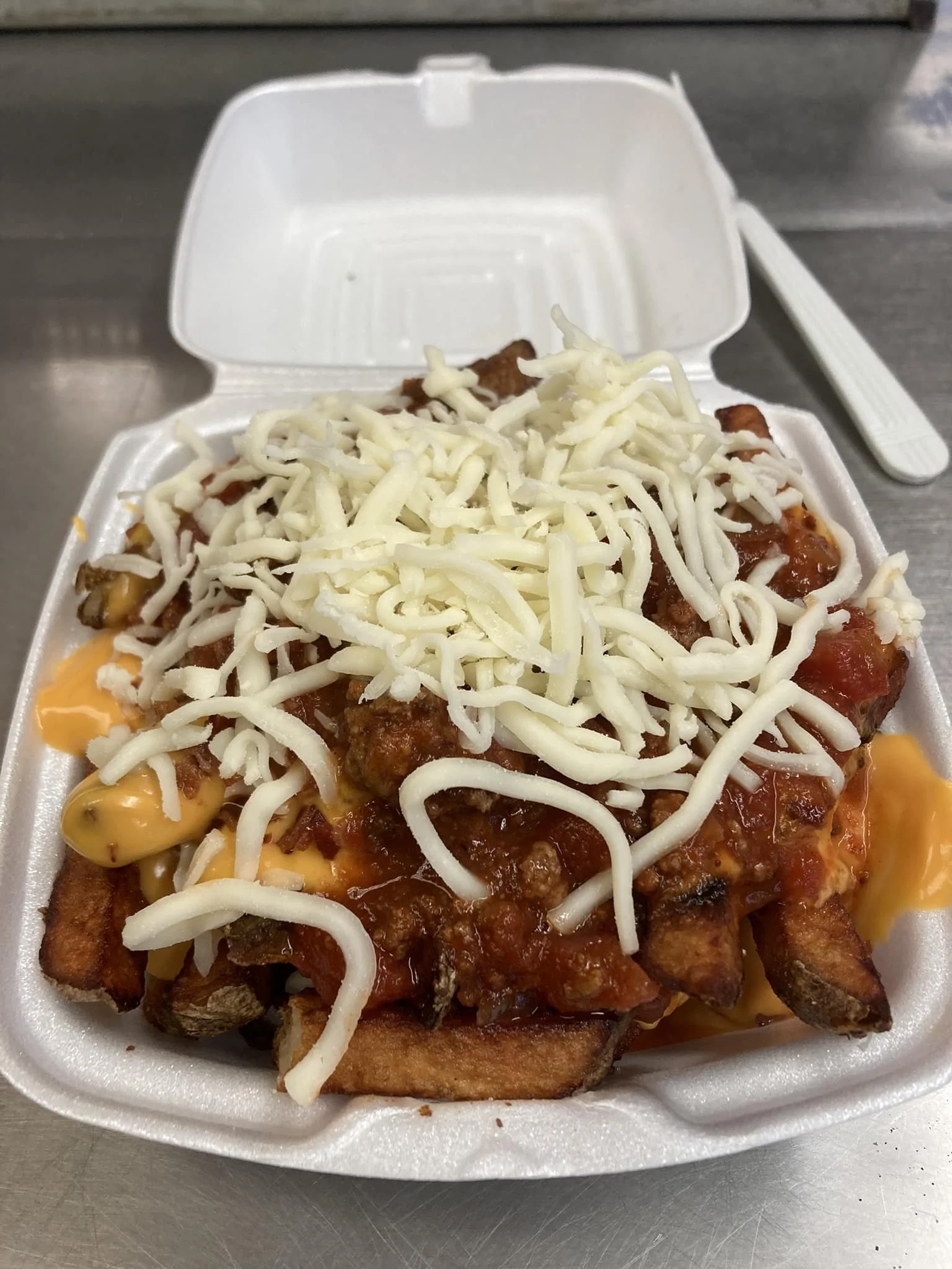 Takeout container filled with loaded french fries topped with shredded cheese, chili, and cheese sauce.