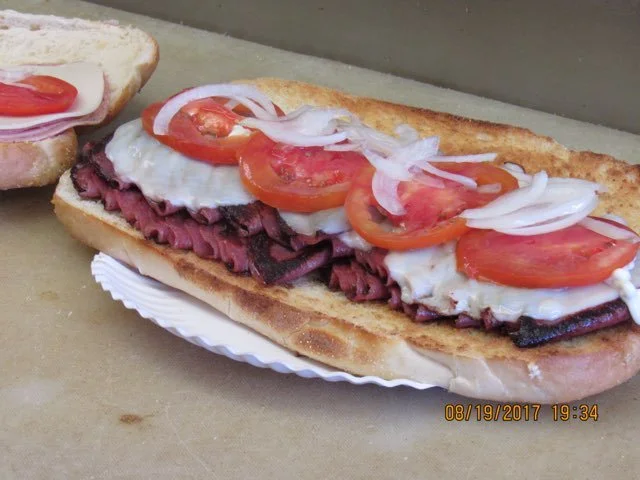 A sub sandwich with sliced tomatoes, onions, lettuce, and roast beef on a toasted hoagie bun.