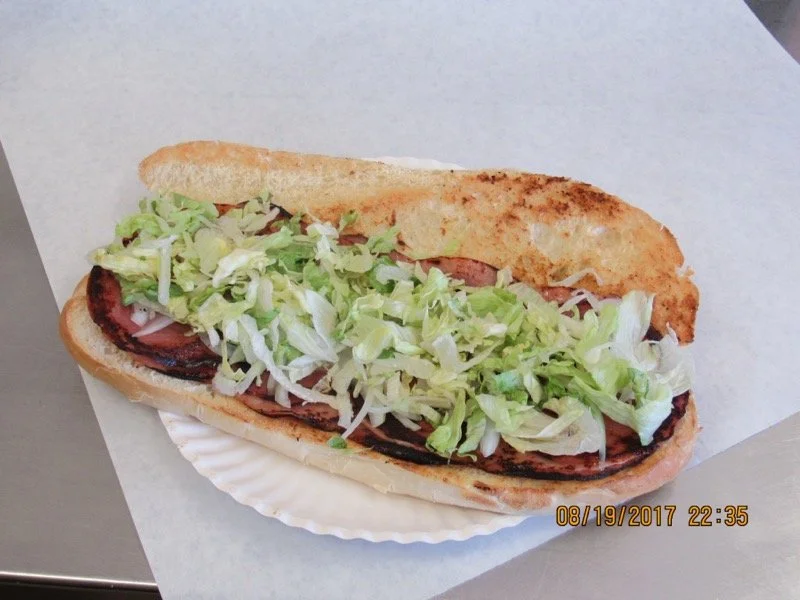 Lettuce and tomato sandwich on a toasted bun with a side of grilled meat, served on a paper plate.