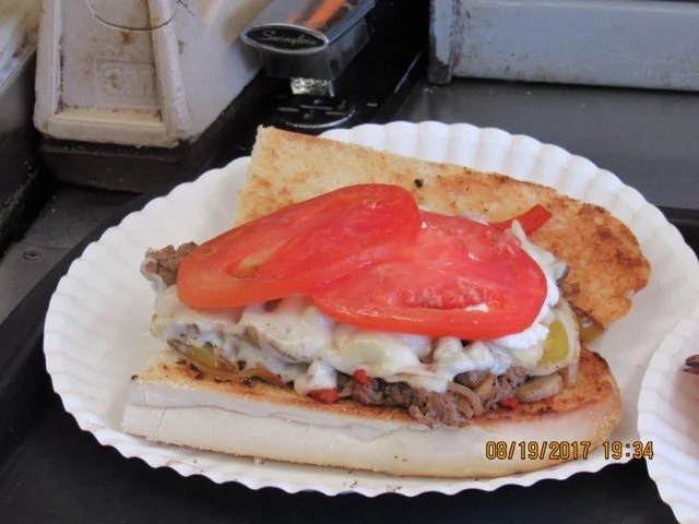 Philly cheesesteak sandwich with tomato and fried potato on a paper plate