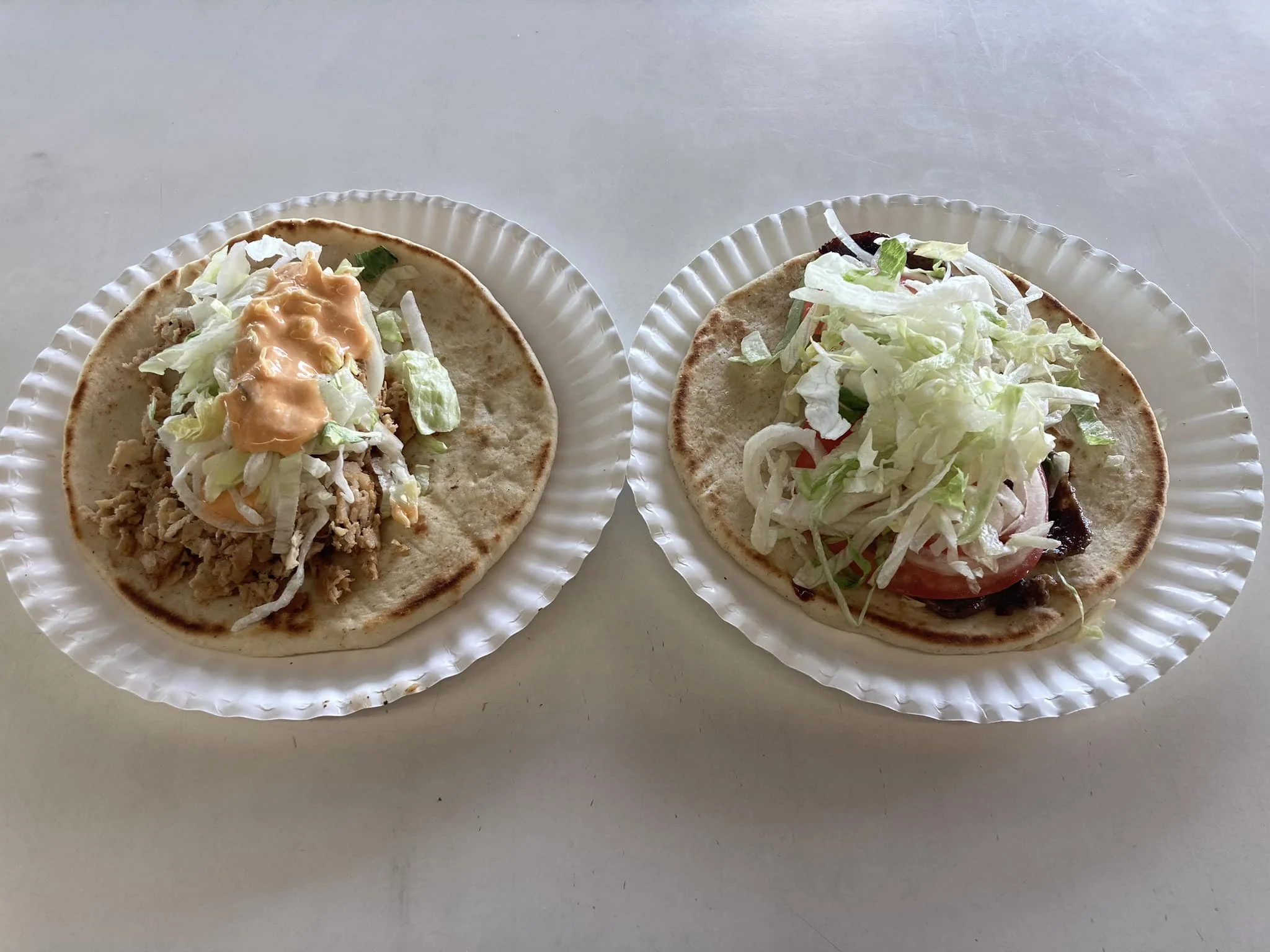 Two tacos on paper plates with lettuce and various toppings