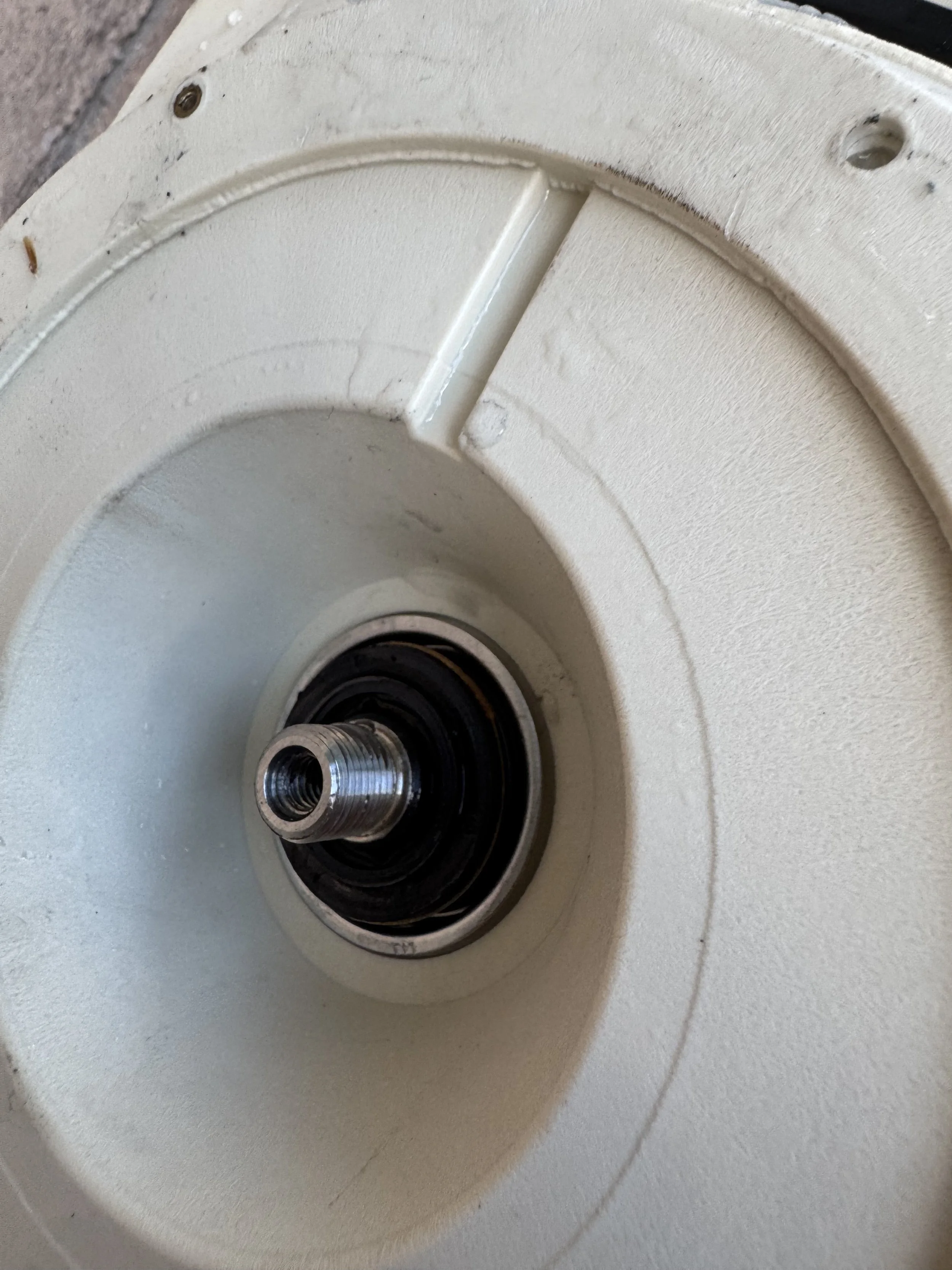 Close-up of a white object with a central metal component, possibly a mechanical part or electronic device, showing some wear and dirt.