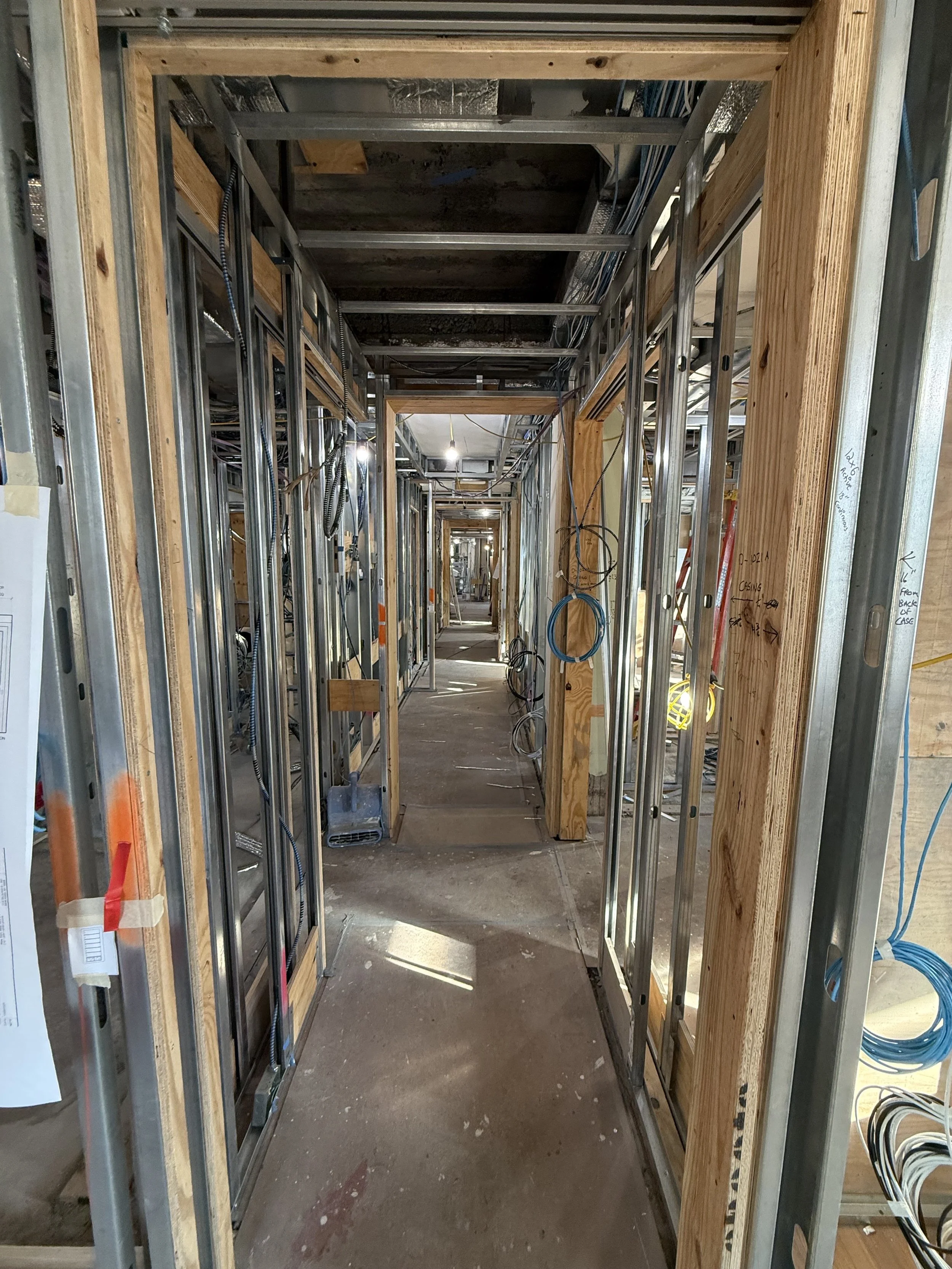 Construction site hallway with metal framing and electrical wiring in progress.