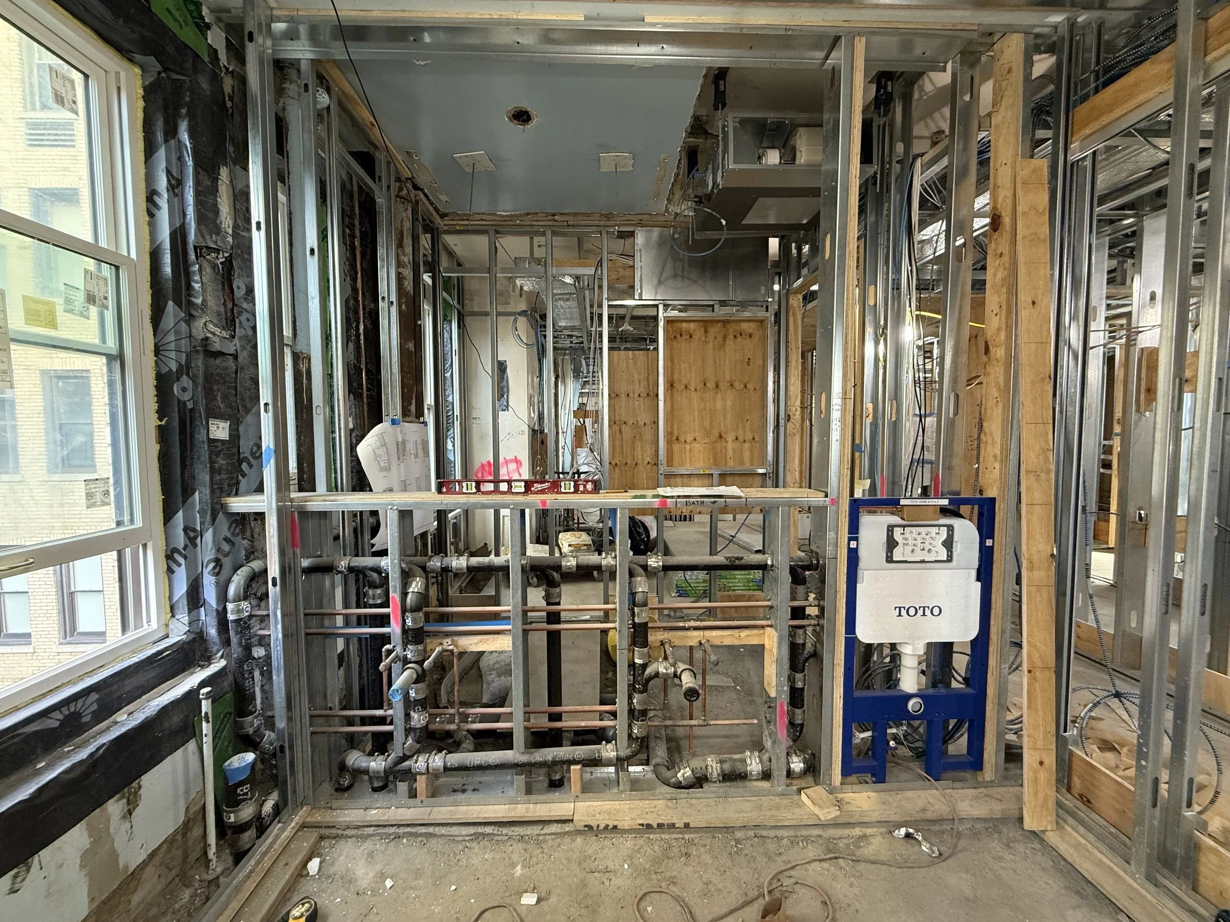 Construction site in a building with exposed metal framing, plumbing pipes, and an in-progress bathroom with a ToTo toilet installation.