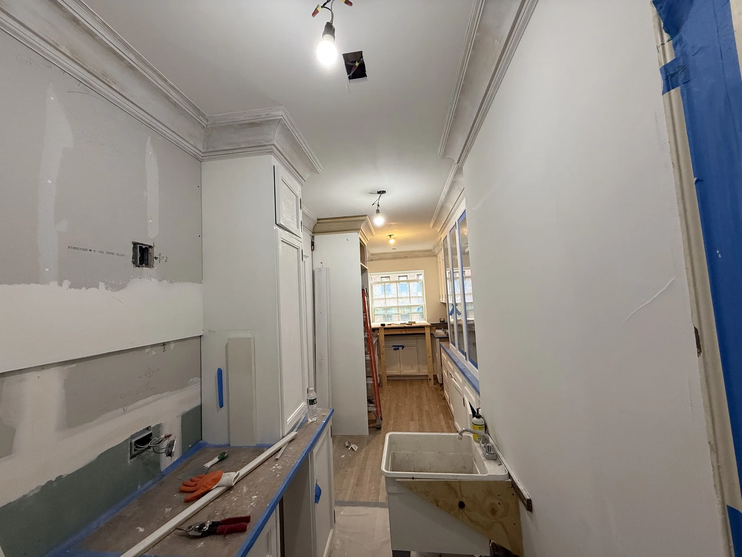 Kitchen under renovation with exposed wiring and unfinished cabinets, a sink, and construction tools.