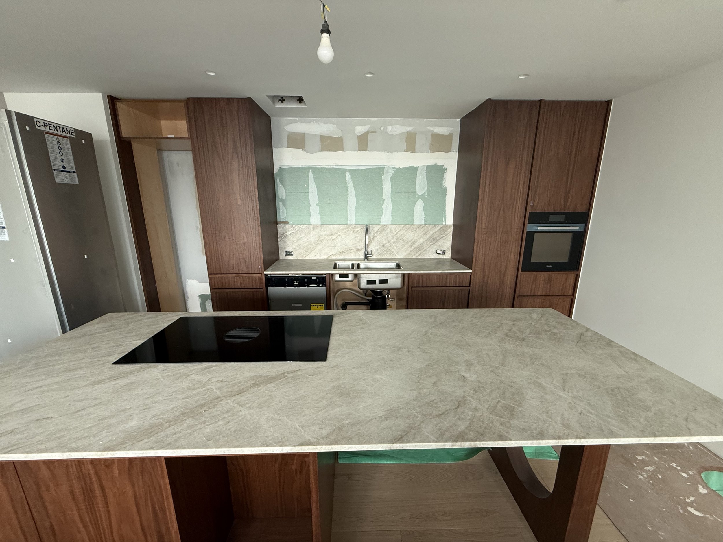 Kitchen under renovation with unfinished drywall, wooden cabinets, marble countertop, stovetop, and oven.