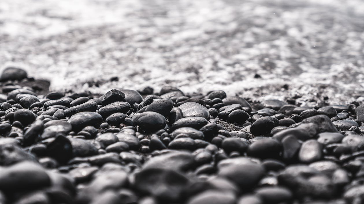 Close-up of black pebbles on a beach with gentle waves in the background.