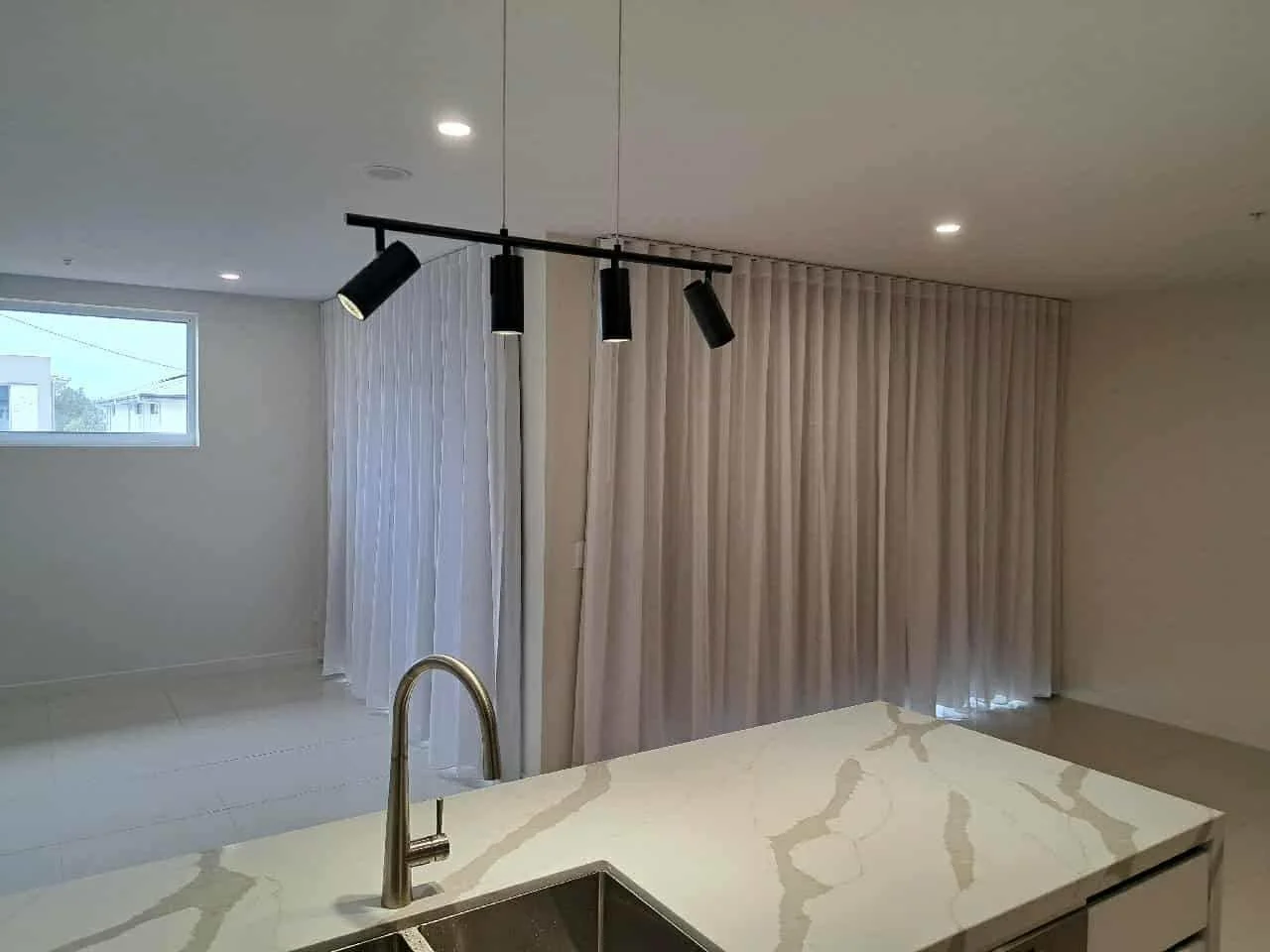Modern kitchen with a marble countertop, standing sink, light-colored curtains, a window, and black ceiling-mounted track lighting.
