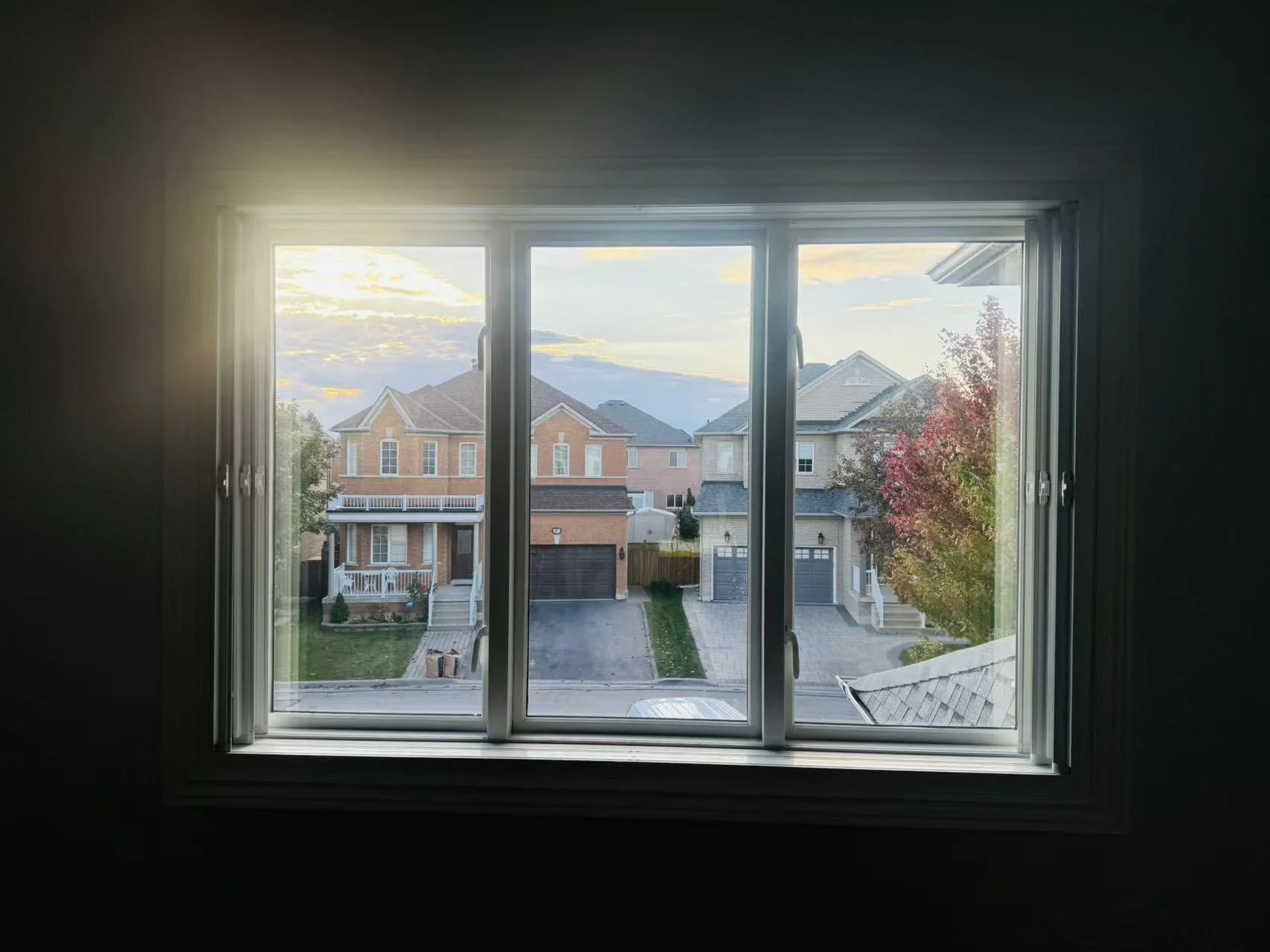 View of suburban houses and trees through a window at sunset.